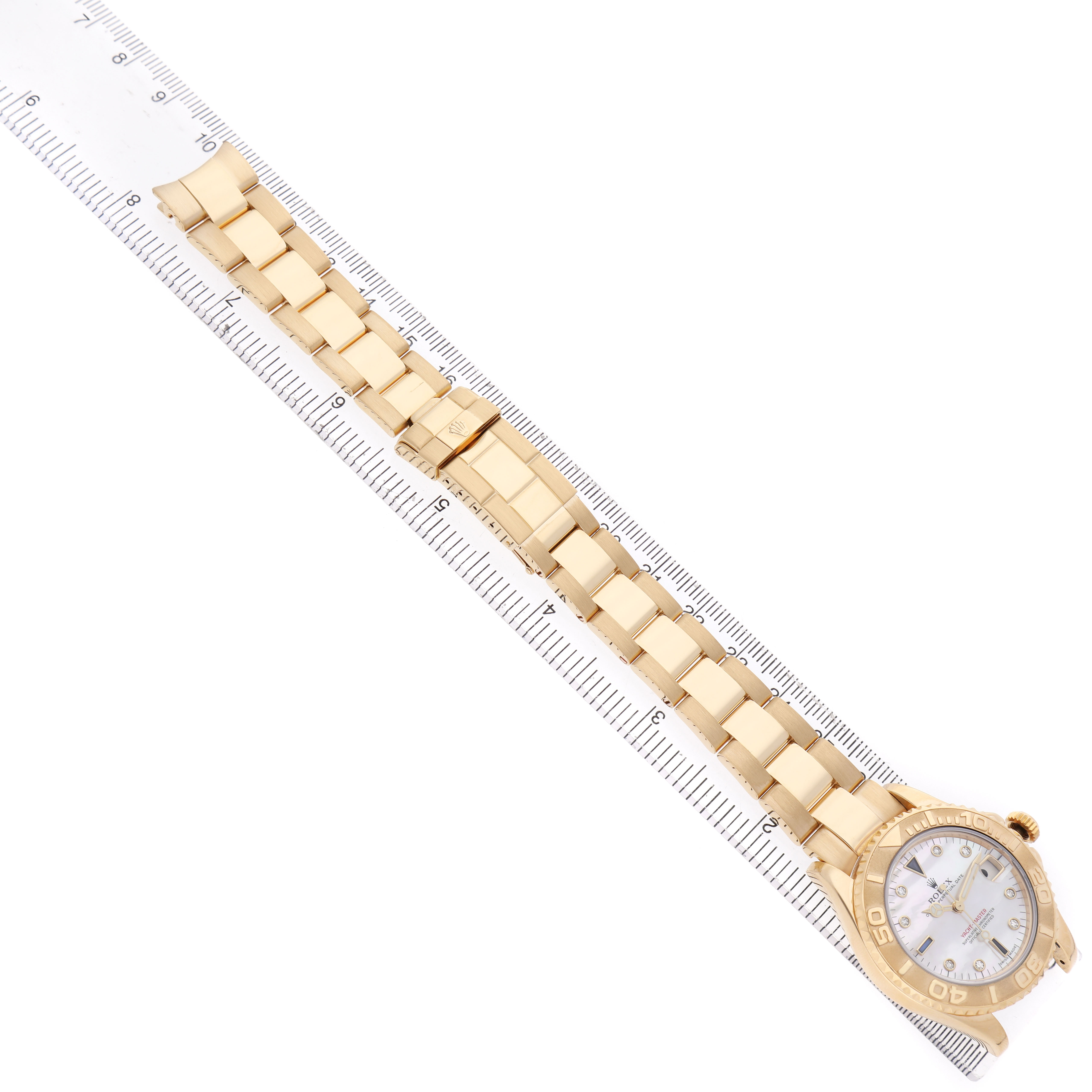 The Rolex Yacht-Master 168628 Women's Yellow Gold Mother of Pearl Dial watch is displayed at an overhead angle, showing the full bracelet, case, and face placed alongside a ruler.