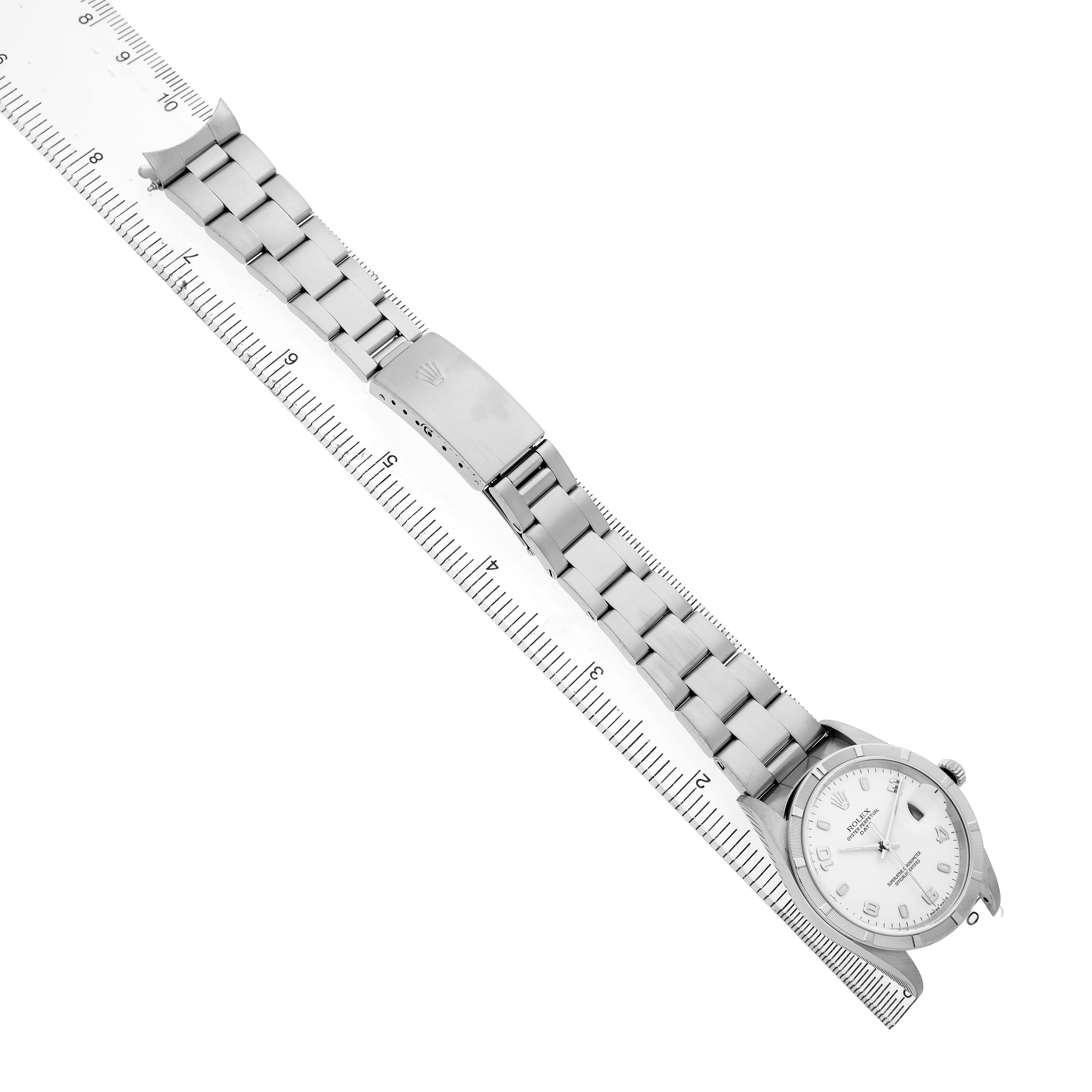 The Rolex Date 15210 Men's Stainless Steel White Dial watch is shown from a top-down angle, displaying the face, bracelet, clasp, and partial links, aligned with a ruler.