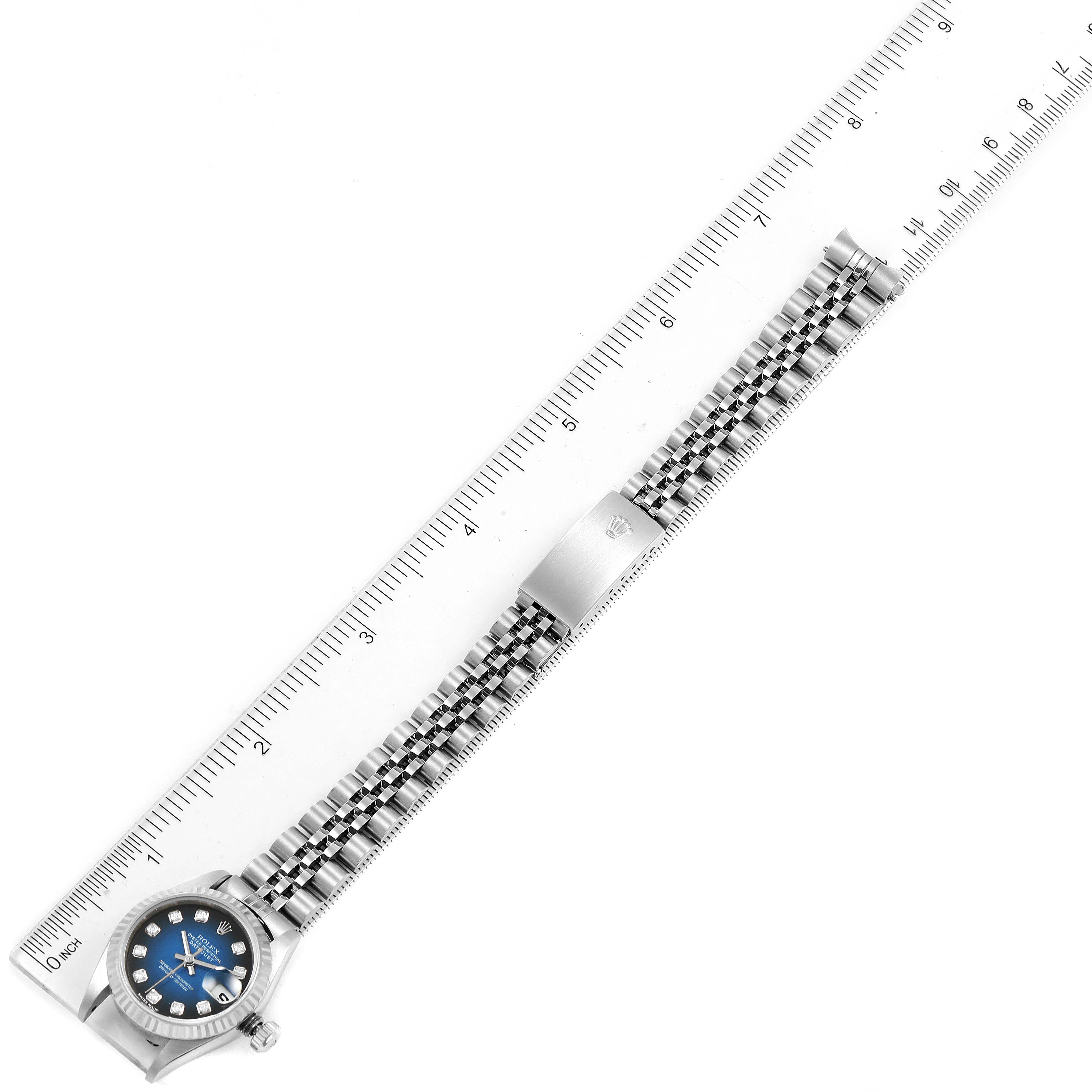 This image shows the entire Rolex Datejust 79174 Women's Stainless Steel Blue Dial 79174 Women's Stainless Steel Blue Dial watch laid flat, with a focus on its band and face, next to a ruler for size reference.