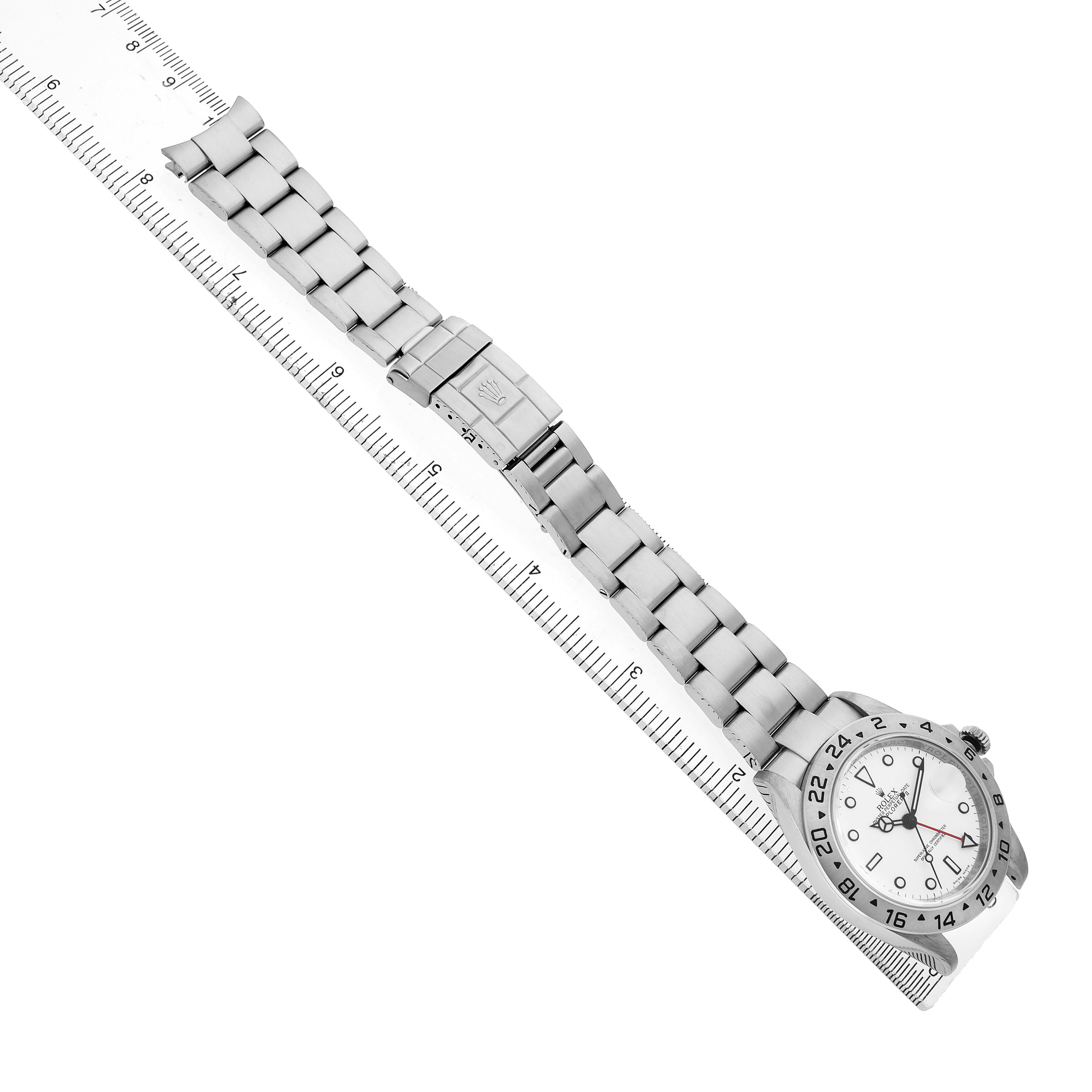 The Rolex Explorer 16570 Men's Stainless Steel White Dial watch is shown from a top view, displaying the face, bracelet, and clasp alongside a ruler for scale.