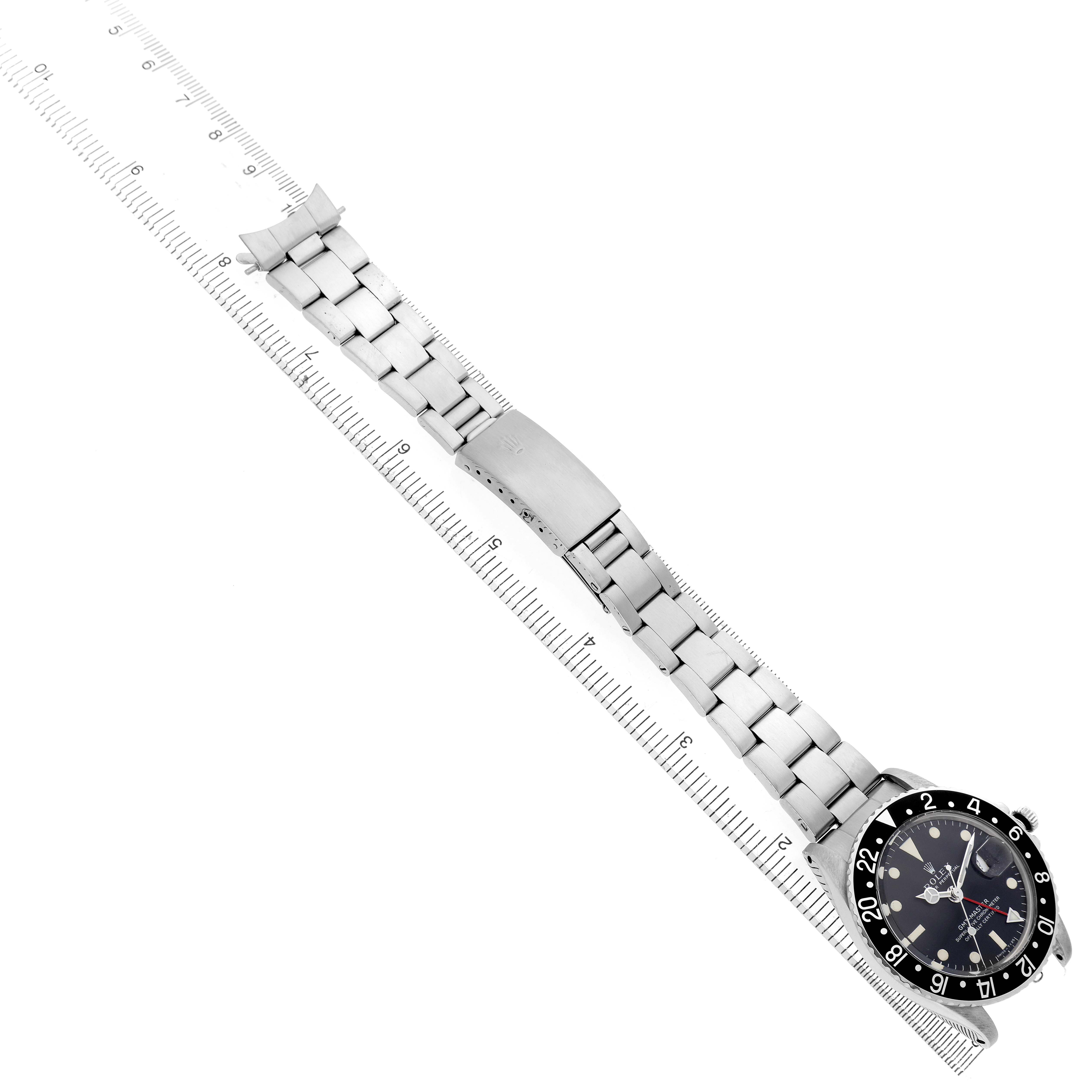 The Vintage Collection Rolex watch is displayed diagonally, showing its black bezel, dial, and metal bracelet on a measuring ruler.