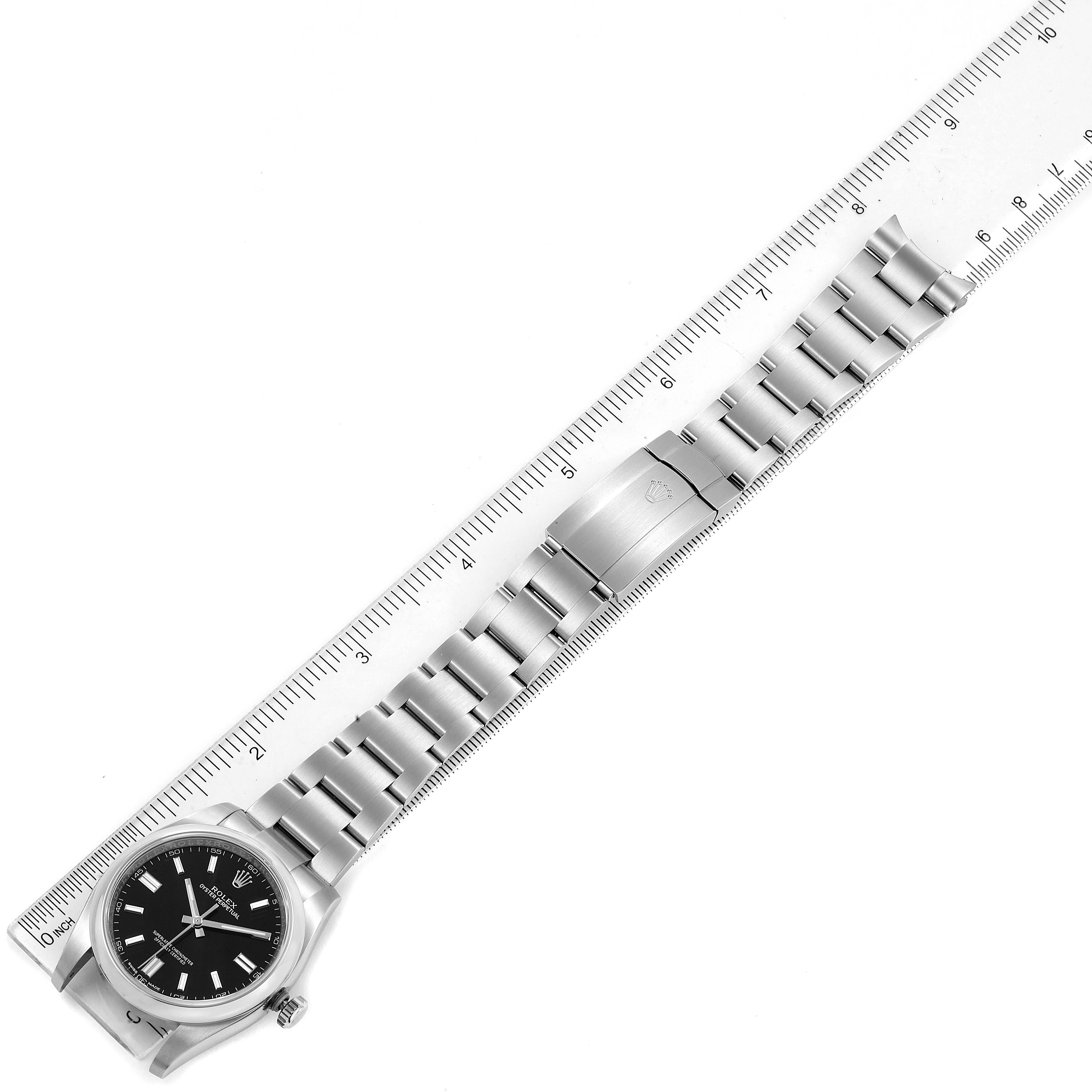 The image shows a Rolex Oyster Perpetual 116000 Men
s Stainless Steel Black Dial 116000 Men
s Stainless Steel Black Dial watch laid flat alongside a ruler, displaying the watch face, bracelet, and clasp.