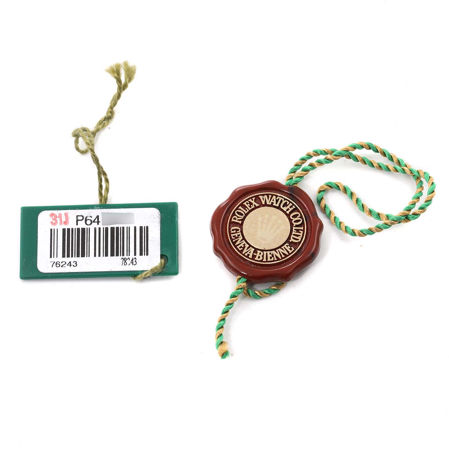 The image shows accessories of a Rolex Oyster Perpetual 76243 Women's Steel and Gold (two tone) Grey Dial 76243 Women's Steel and Gold (two tone) Grey Dial, specifically a green tag with a barcode and a red seal with a string.