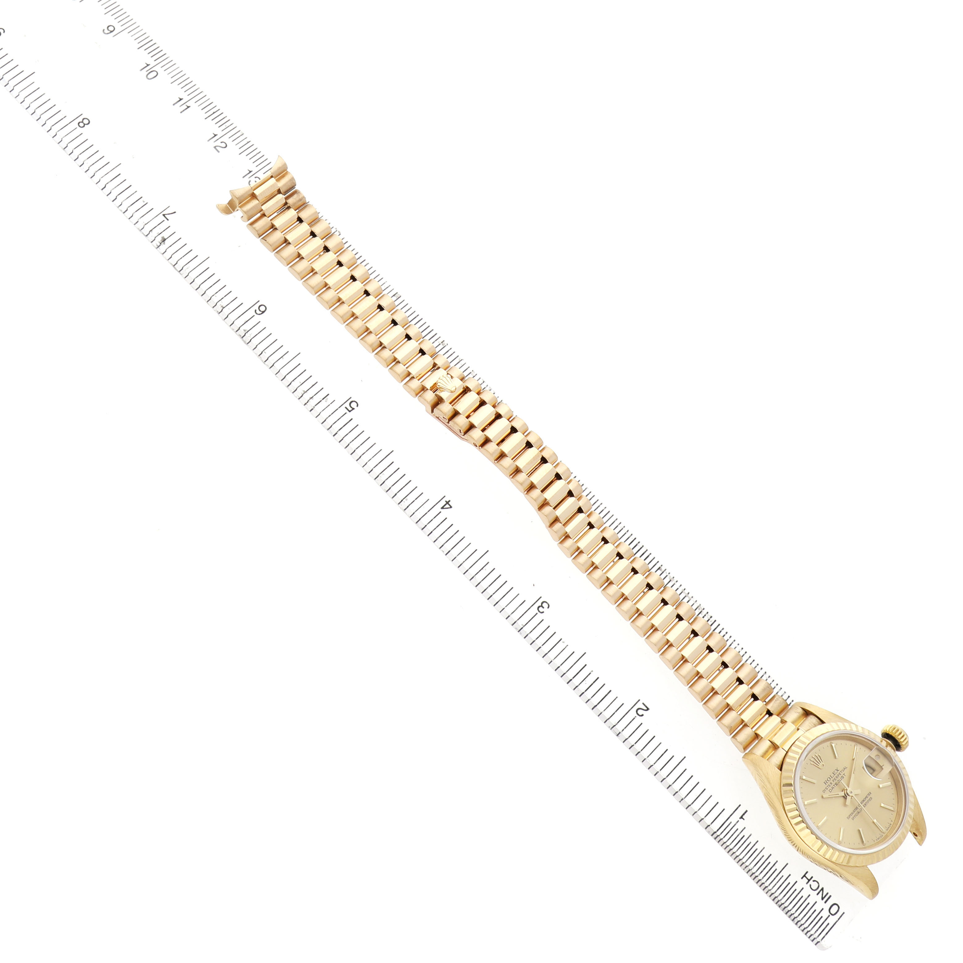 The Rolex President 69178 Women's Yellow Gold Champagne Dial watch is shown from an overhead angle, featuring its bracelet and face beside a ruler.