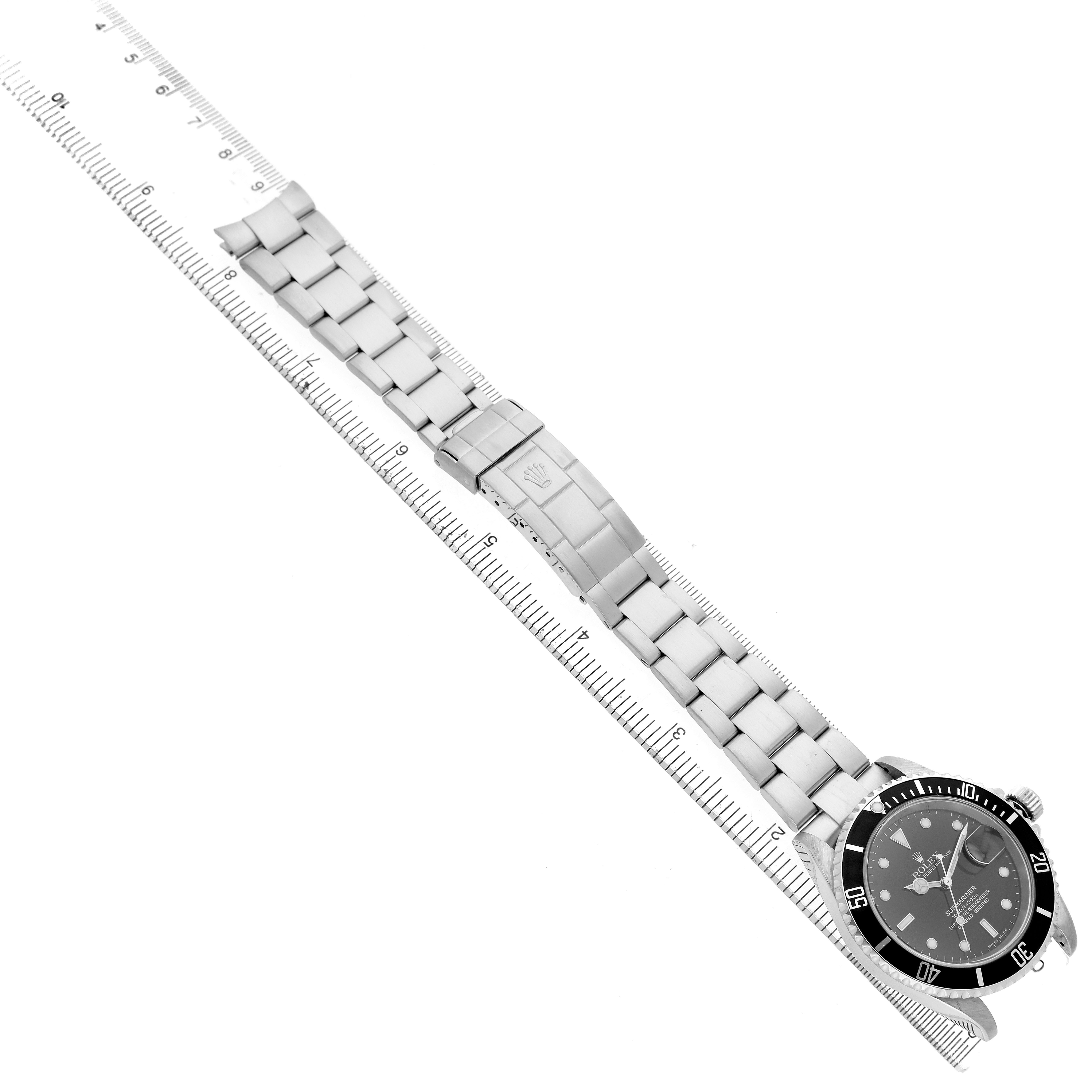 The Rolex Submariner 16610 Men's Stainless Steel Black Dial watch is shown in an overhead view with its bracelet fully visible, placed along a ruler for scale.