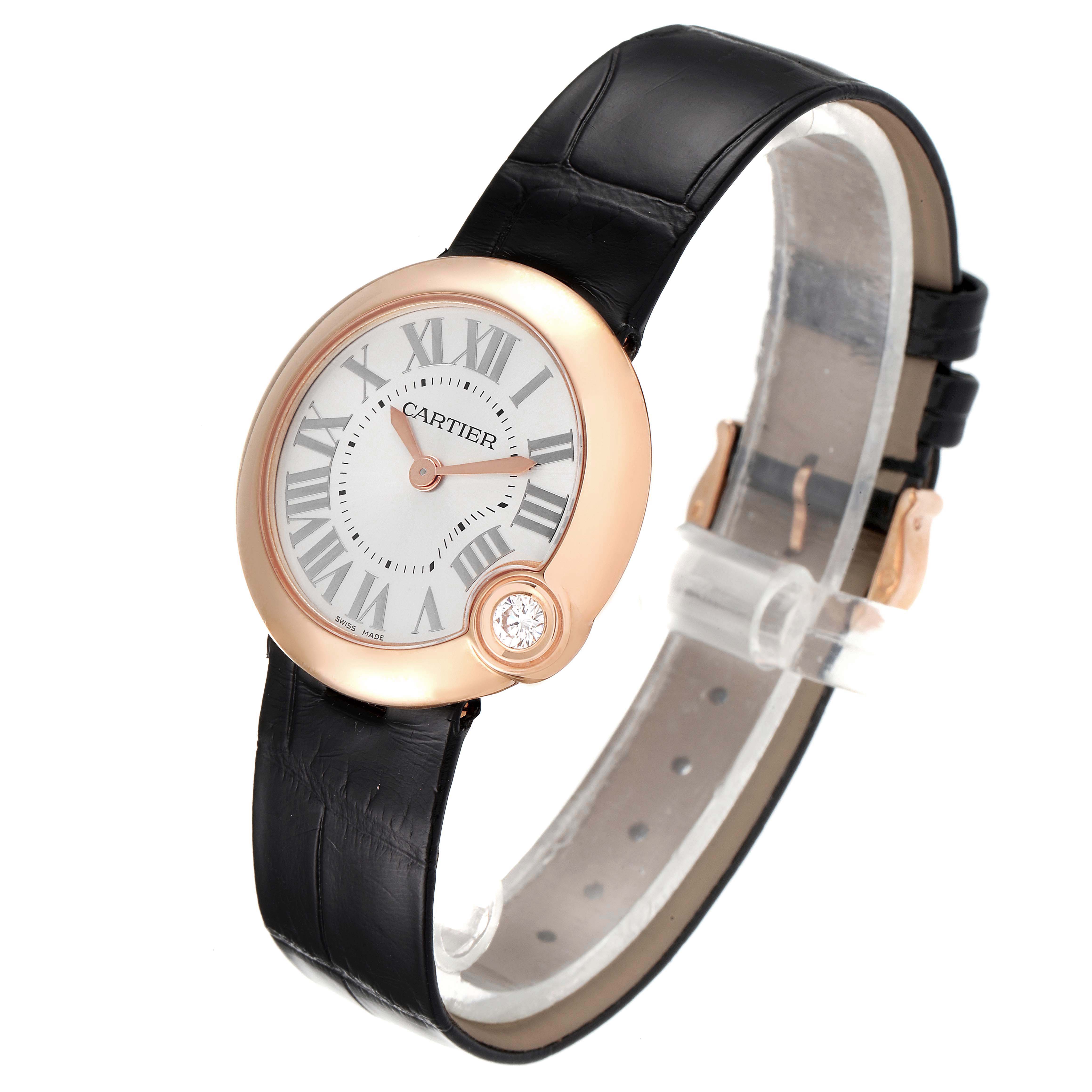 The Ballon Bleu by Cartier is shown at a slight angle highlighting its rose gold case, white dial, black leather strap, and a diamond detail.