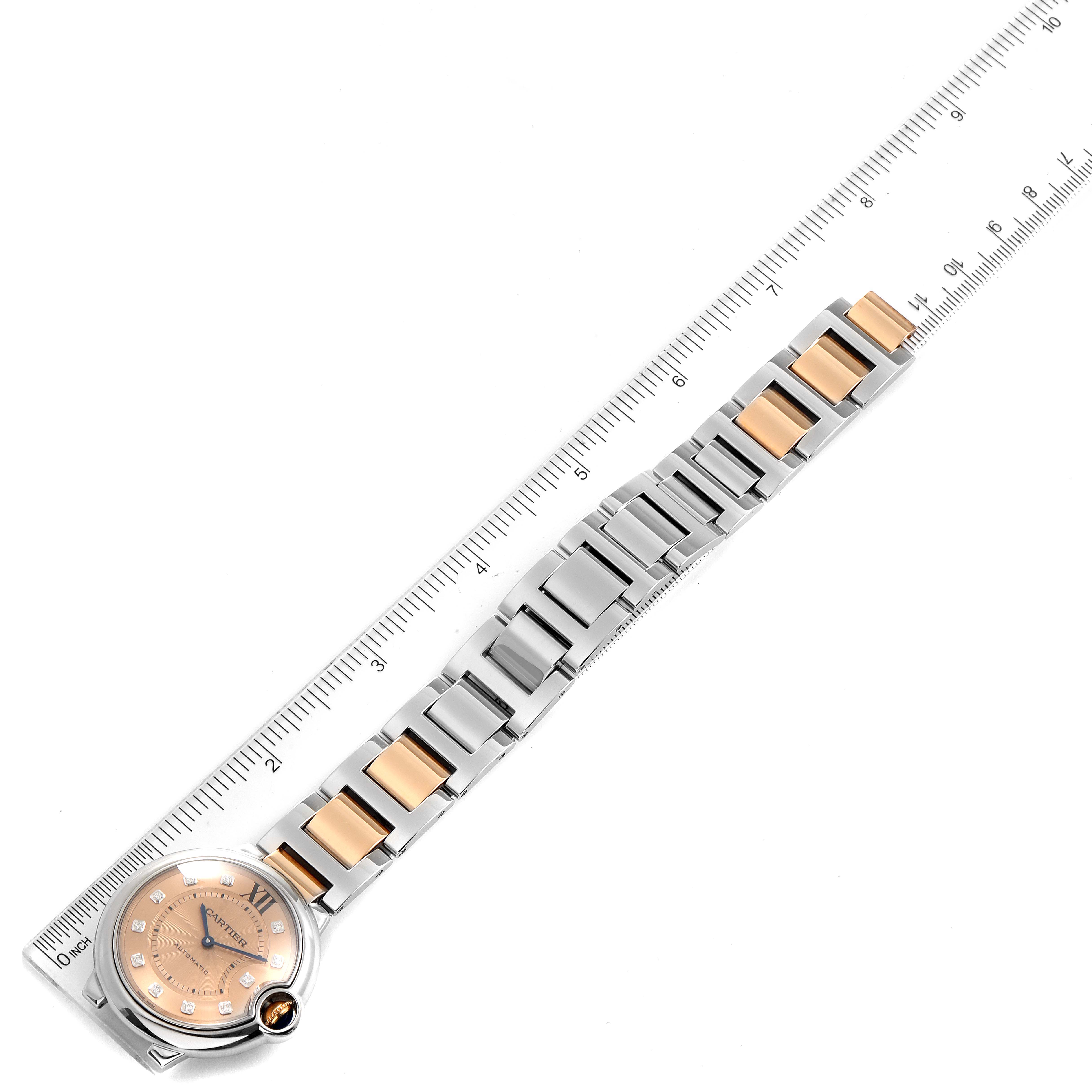 This image shows the Cartier Ballon Bleu WE902054 Women's Steel and Gold (two tone) Pink Dial WE902054 Women's Steel and Gold (two tone) Pink Dial watch laid flat next to a ruler, highlighting its bracelet and dial.