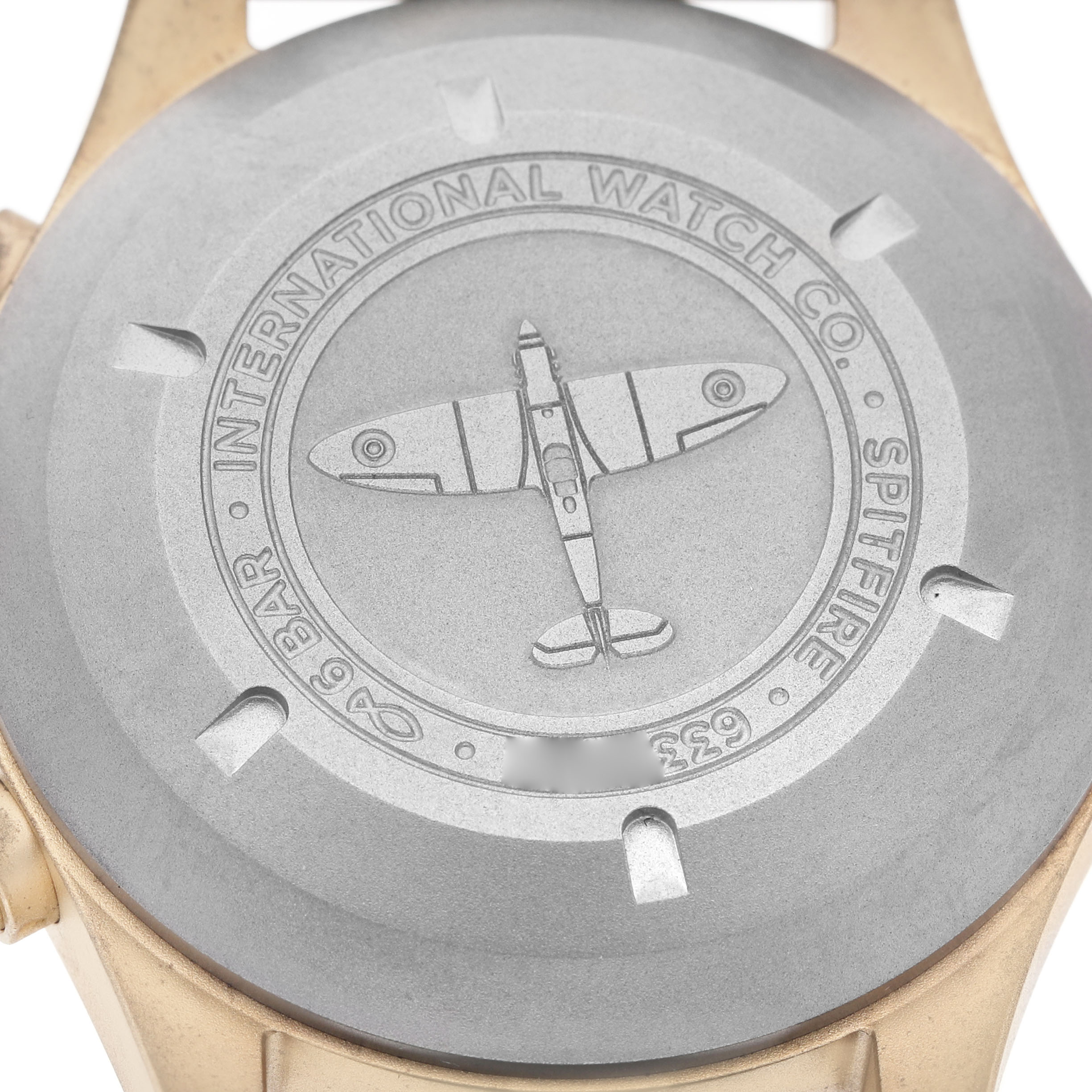 The image shows the case back of an IWC Pilot IW387902 Men's Bronze Green Dial watch, featuring an engraved Spitfire airplane and branding details.