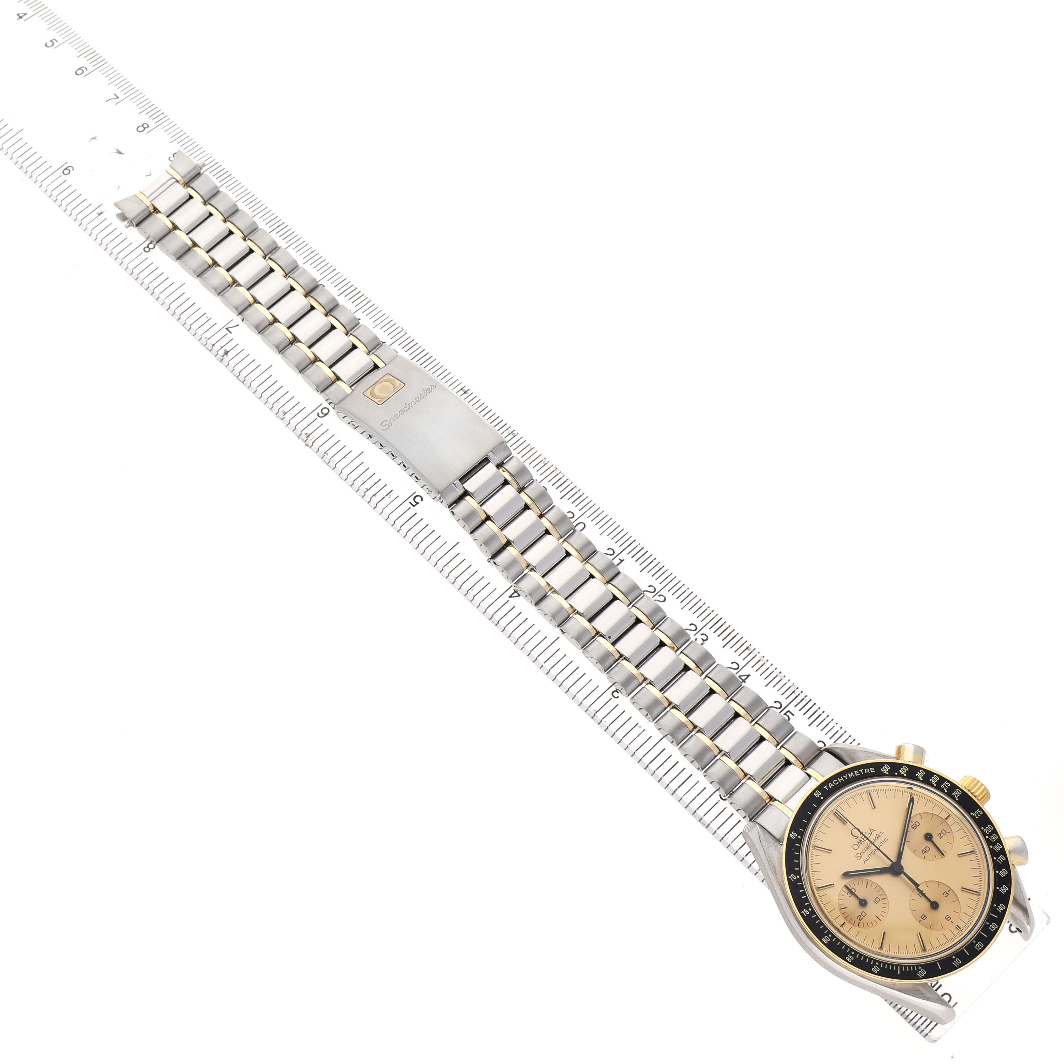 The Omega Speedmaster 3310.10.00 Men's Steel and Gold (two tone) Champagne Dial watch is shown at an angle, highlighting the dial, bezel, bracelet, and clasp next to a ruler for scale.