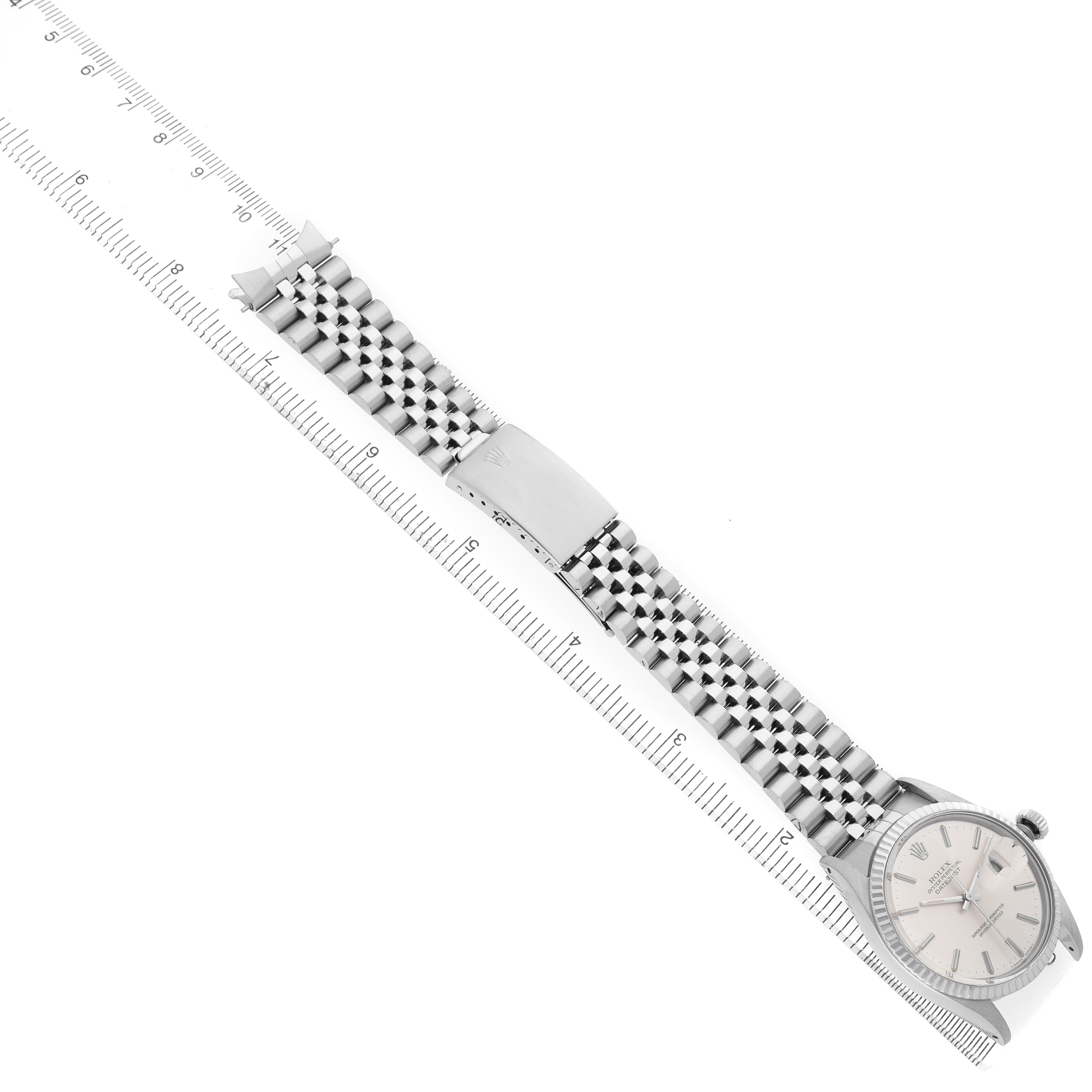 The Rolex Datejust 16014 Men's Stainless Steel Silver Dial watch is shown in a top-down angle, displaying the bracelet and clasp alongside a measuring ruler.