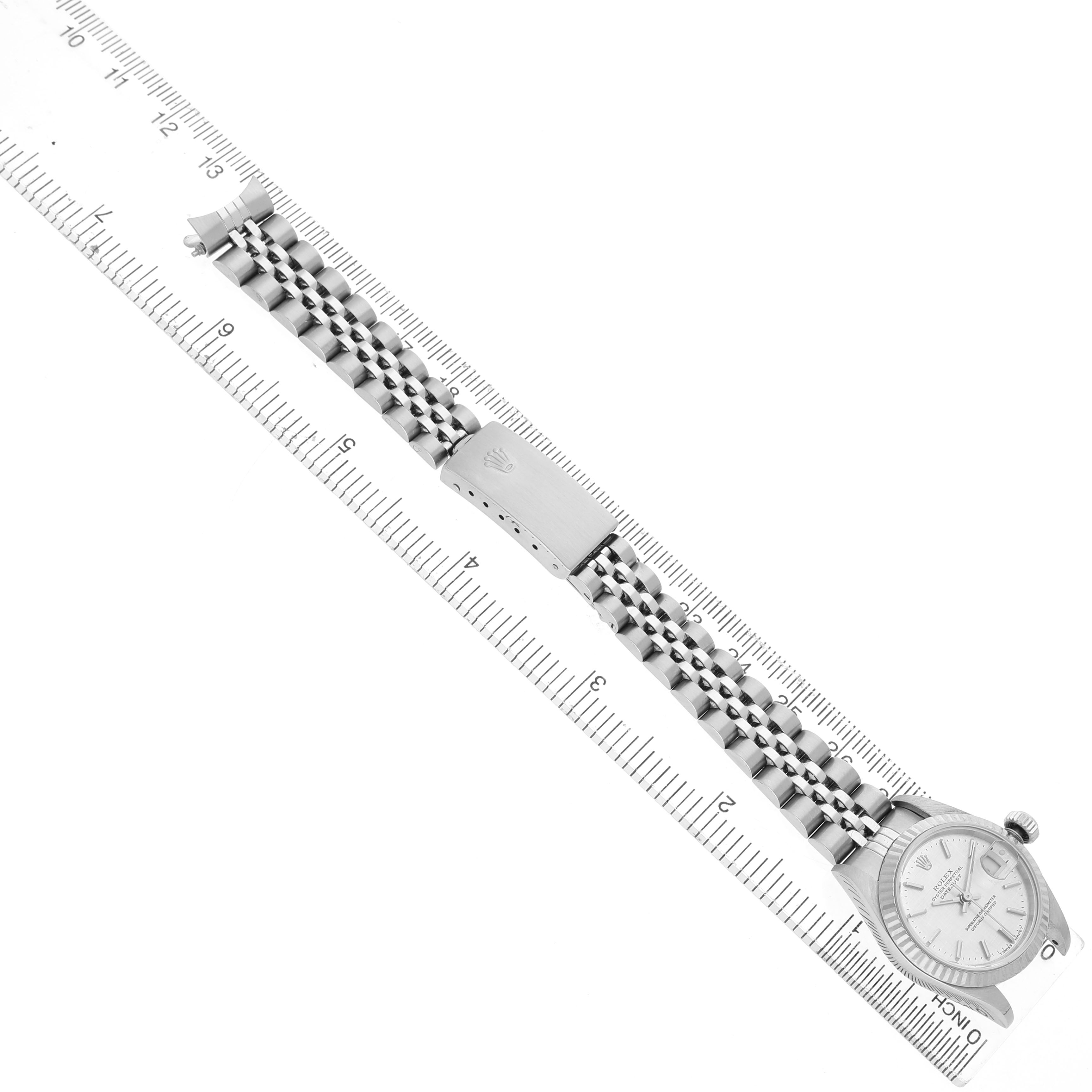 The Rolex Datejust 79174 Women's Stainless Steel Silver Dial watch is shown from a top view at a slight angle, displaying the face and full bracelet, placed alongside a ruler.