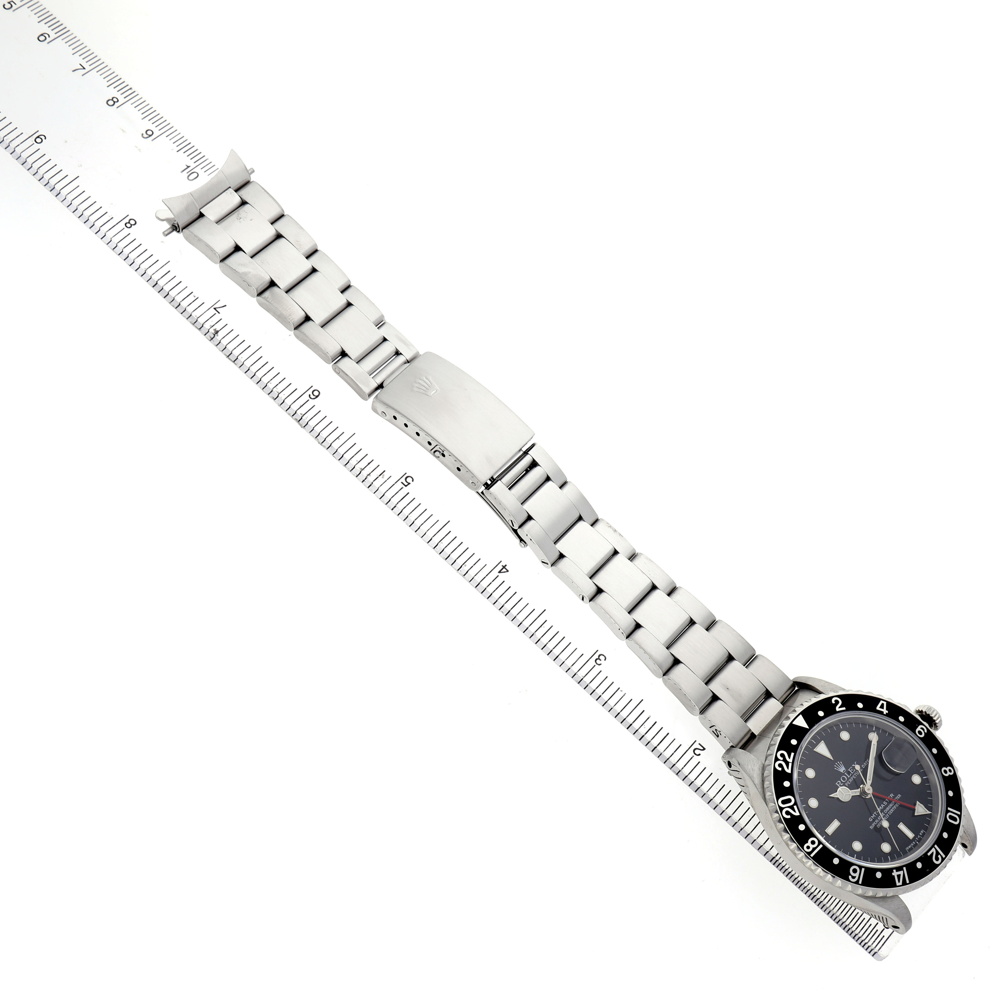 The Rolex GMT-Master 16700 Men's Stainless Steel Black Dial watch is shown laid flat, displaying the face and full metal bracelet against a ruler for scale.