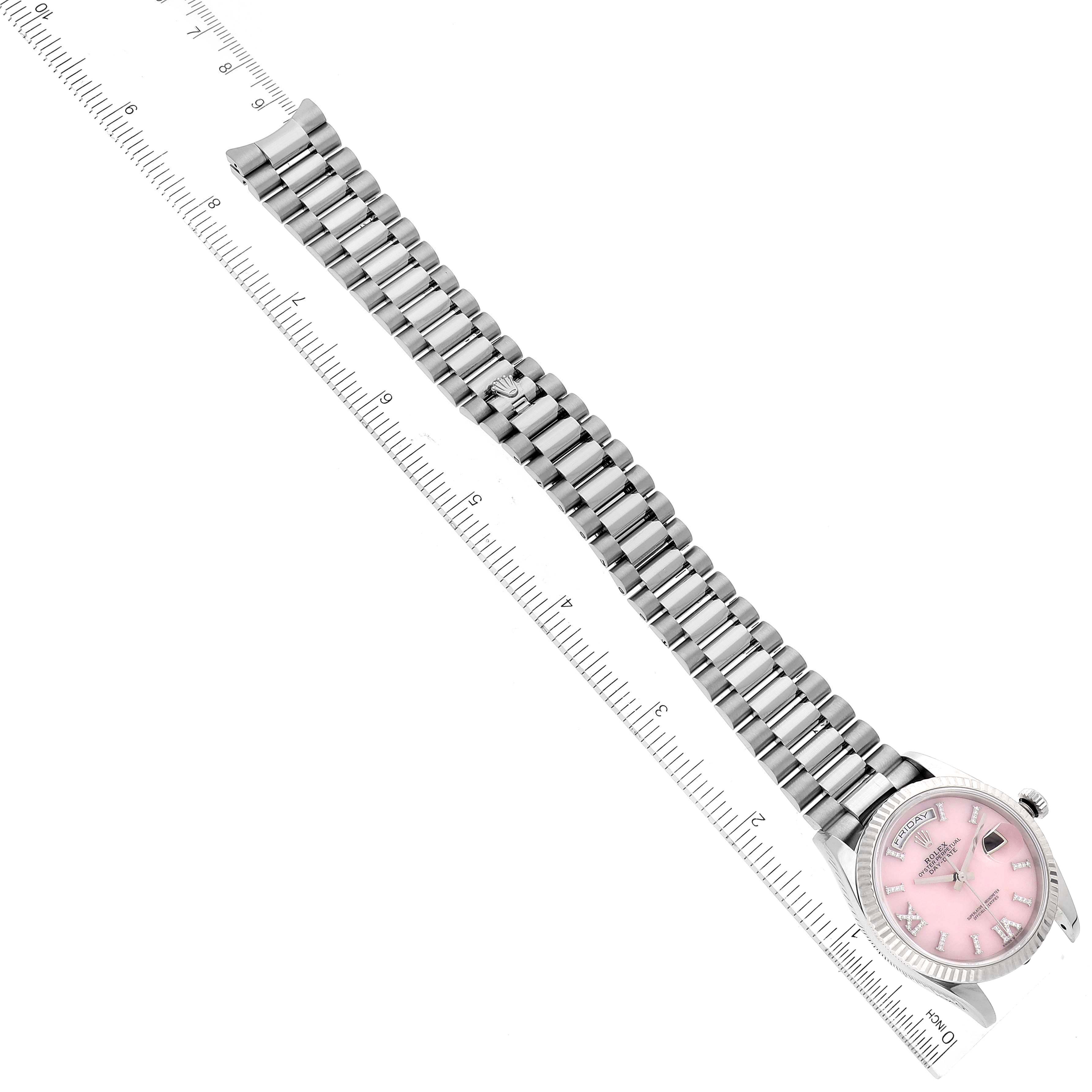 The Rolex President 128239 Men's White Gold Pink Dial 128239 Men's White Gold Pink Dial watch is shown from a top-down angle, highlighting its pink dial and metallic bracelet alongside a ruler.