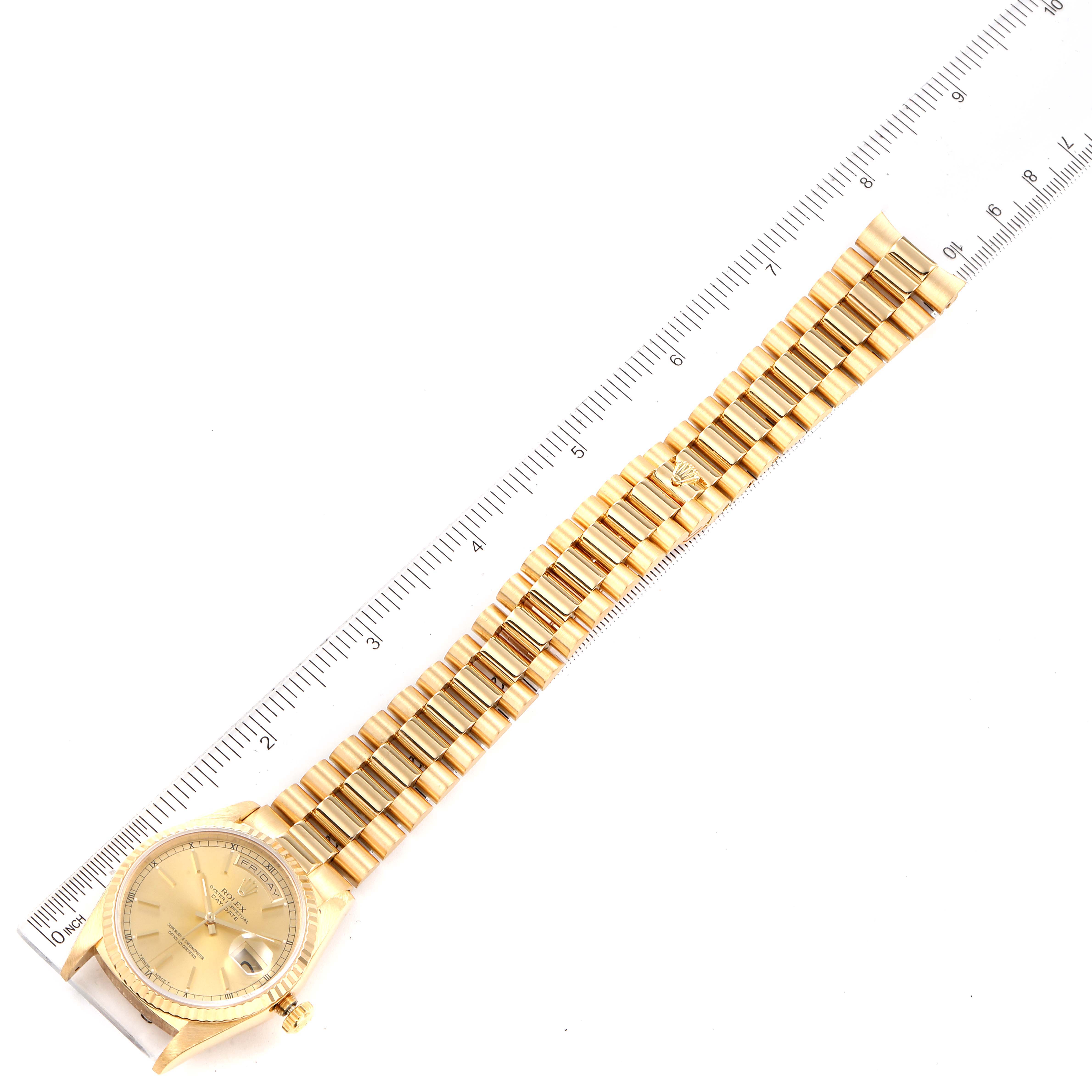 This image shows the Rolex President 18238 Men's Yellow Gold Champagne Dial 18238 Men's Yellow Gold Champagne Dial model watch with its gold band and face, lying flat next to a ruler.
