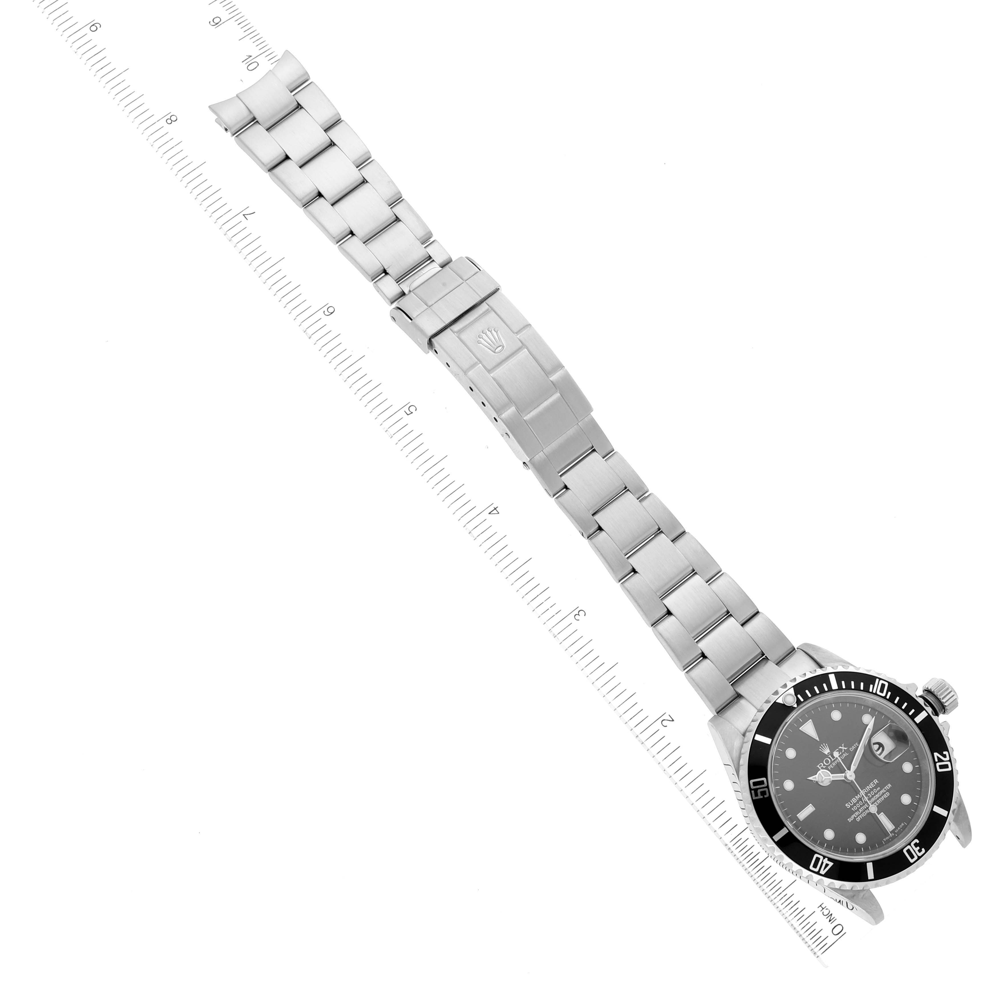 The image shows the Rolex Submariner 16610 Men
s Stainless Steel Black Dial 16610 Men
s Stainless Steel Black Dial watch laid flat with the face and metal bracelet fully visible, positioned along a ruler for scale.
