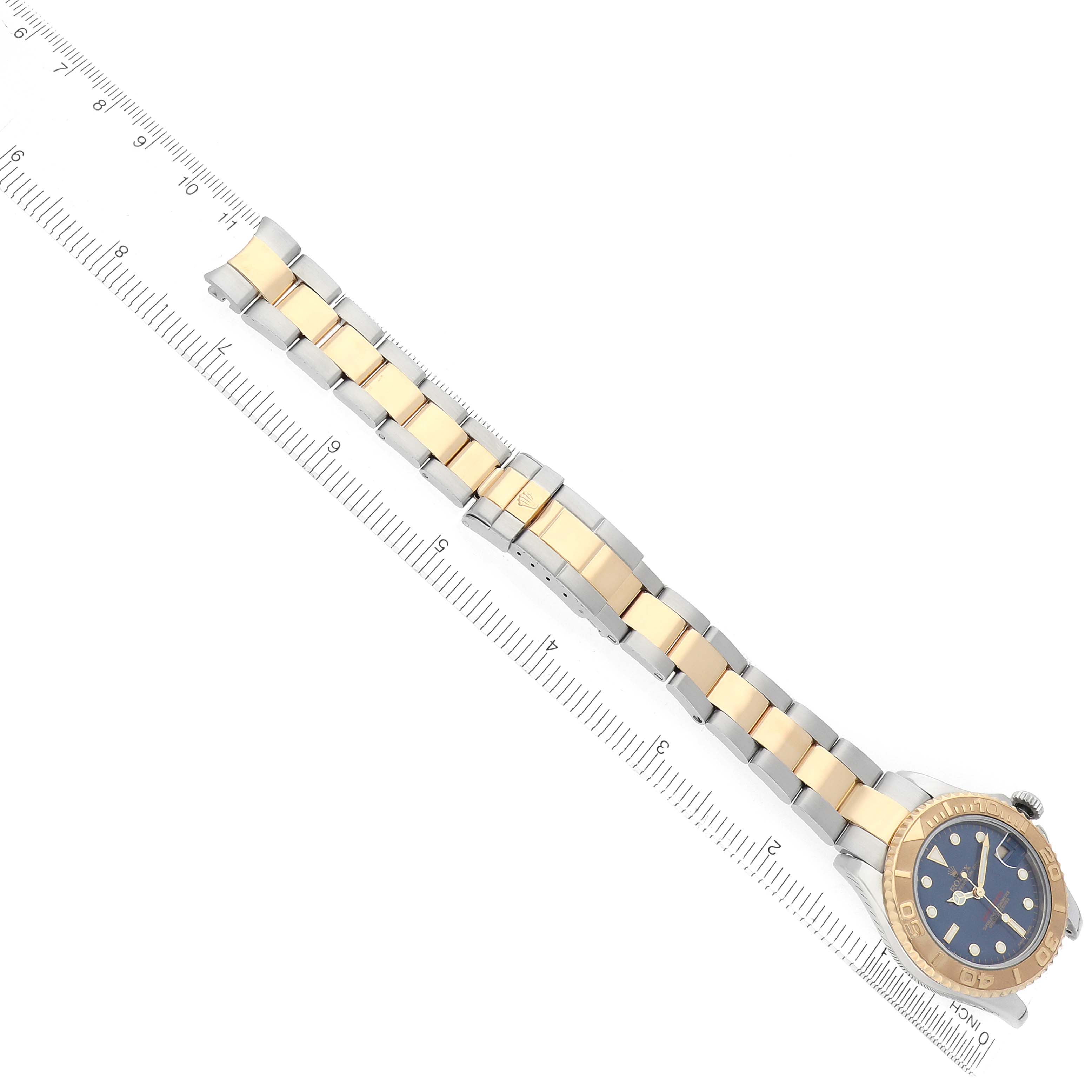 The Rolex Yacht-Master 168623 Men's Steel and Gold (two tone) Blue Dial watch is shown diagonally, displaying its full bracelet and face alongside a measuring ruler.