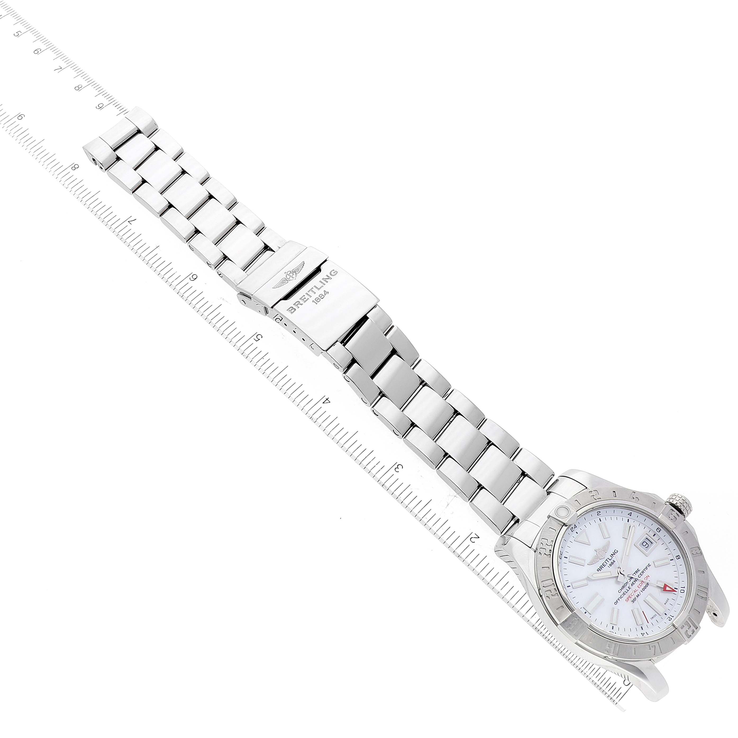 The image shows a Breitling Avenger A32390 Men's Stainless Steel Mother of Pearl Dial A32390 Men's Stainless Steel Mother of Pearl Dial watch laid flat beside a ruler, highlighting the metal bracelet and watch face.
