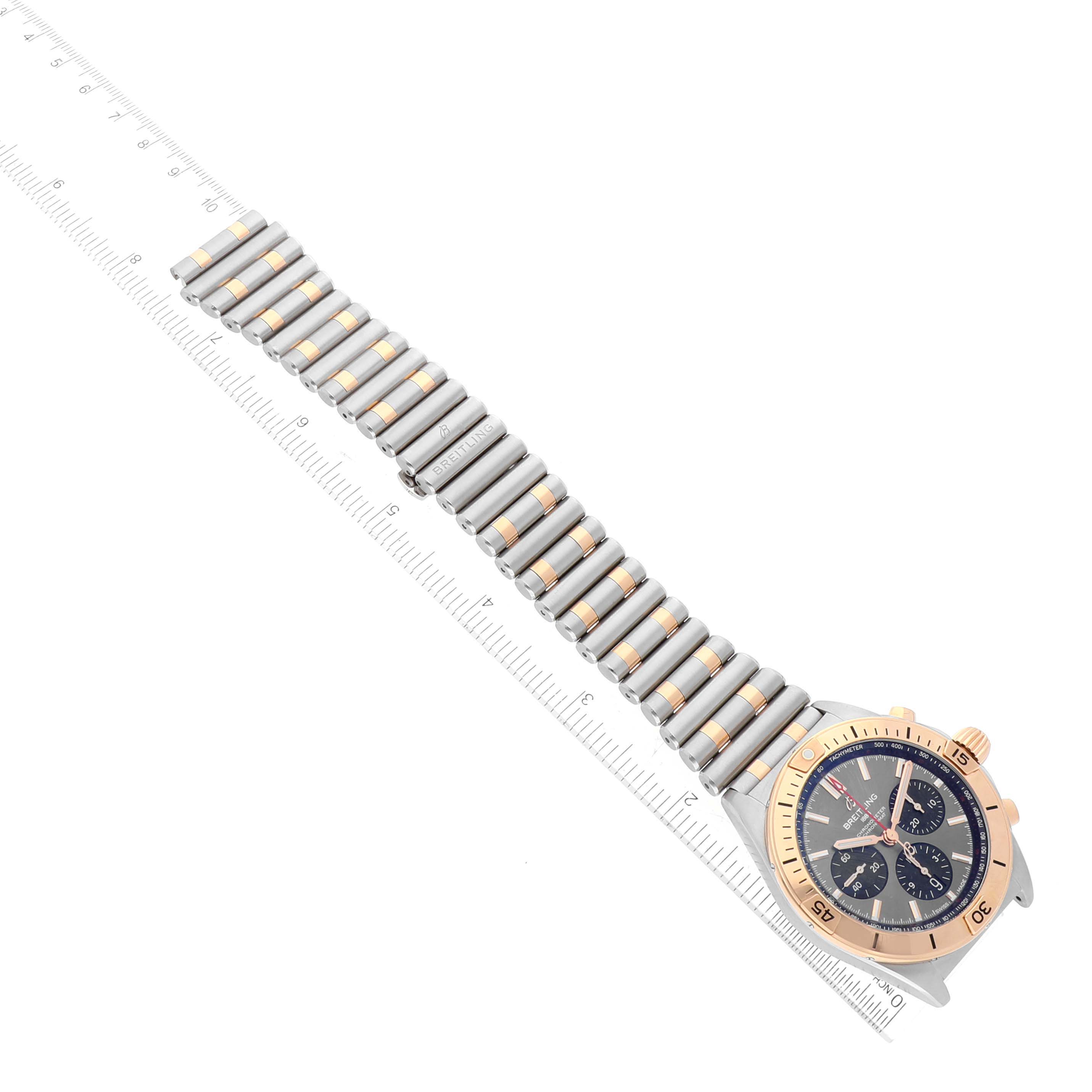 The image displays a top view of a Breitling Chronomat UB0134 Men's Steel and Gold (two tone) Grey Dial UB0134 Men's Steel and Gold (two tone) Grey Dial watch, showcasing its full bracelet and dial, with a ruler for scale.