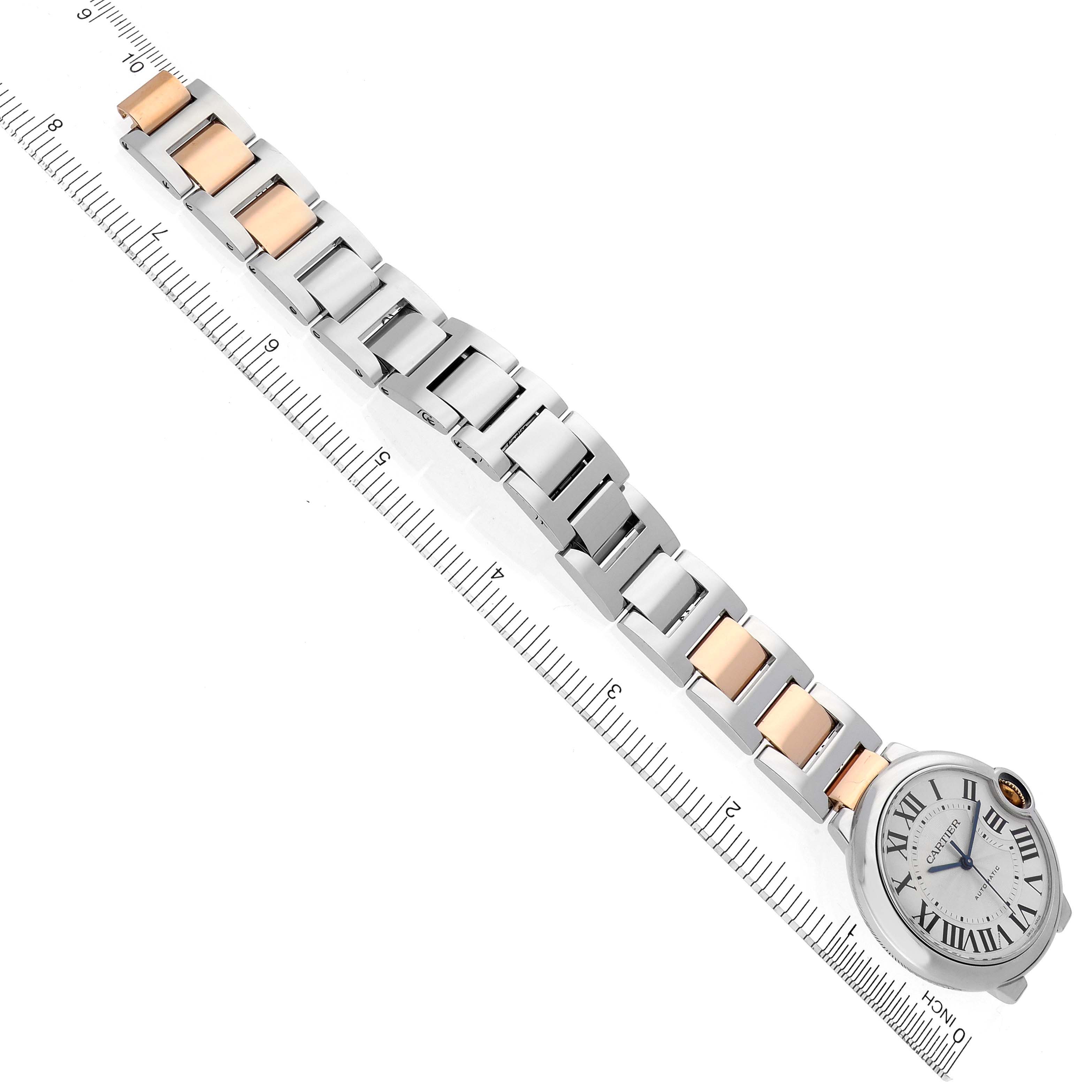 The Ballon Bleu de Cartier watch is shown at an angle, displaying its full metal bracelet and face alongside a ruler.