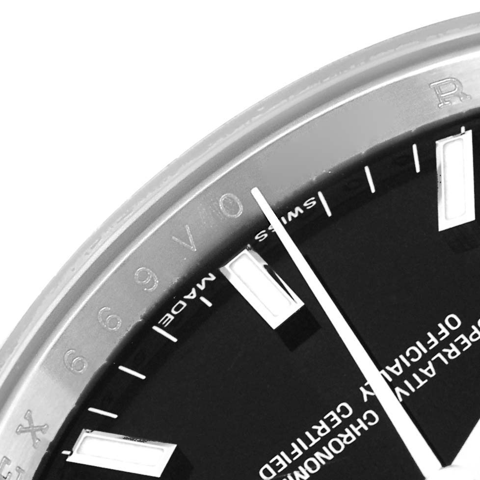 The image shows a close-up of the Rolex Date 115200 Men's Stainless Steel Black Dial 115200 Men's Stainless Steel Black Dial model watch, highlighting part of the dial, hour markers, and second hand.