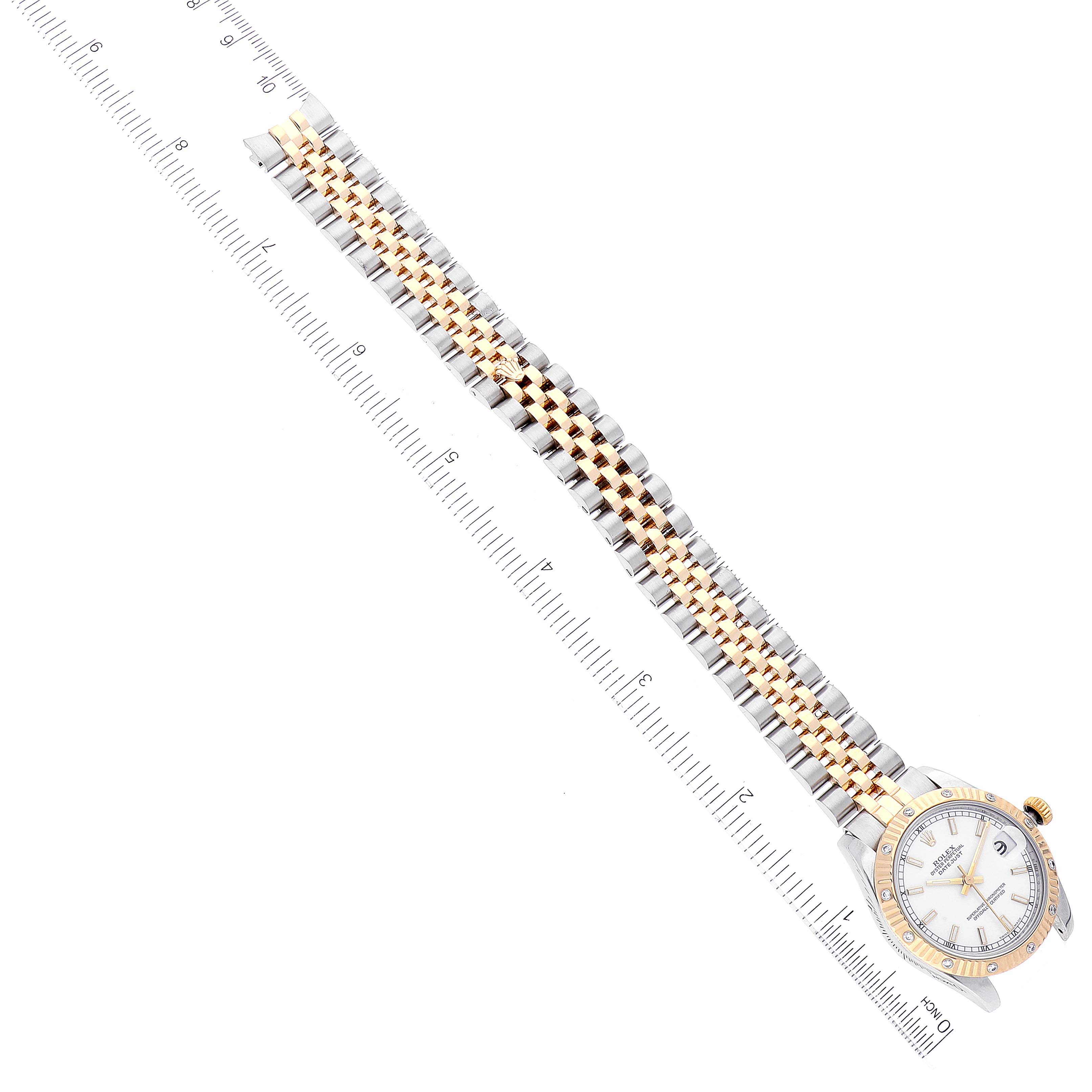The image shows a top-down view of a Rolex Mid-Size 178313 Women
s Steel and Gold (two tone) White Dial 178313 Women
s Steel and Gold (two tone) White Dial model watch, highlighting its two-tone metal bracelet and face next to a ruler.