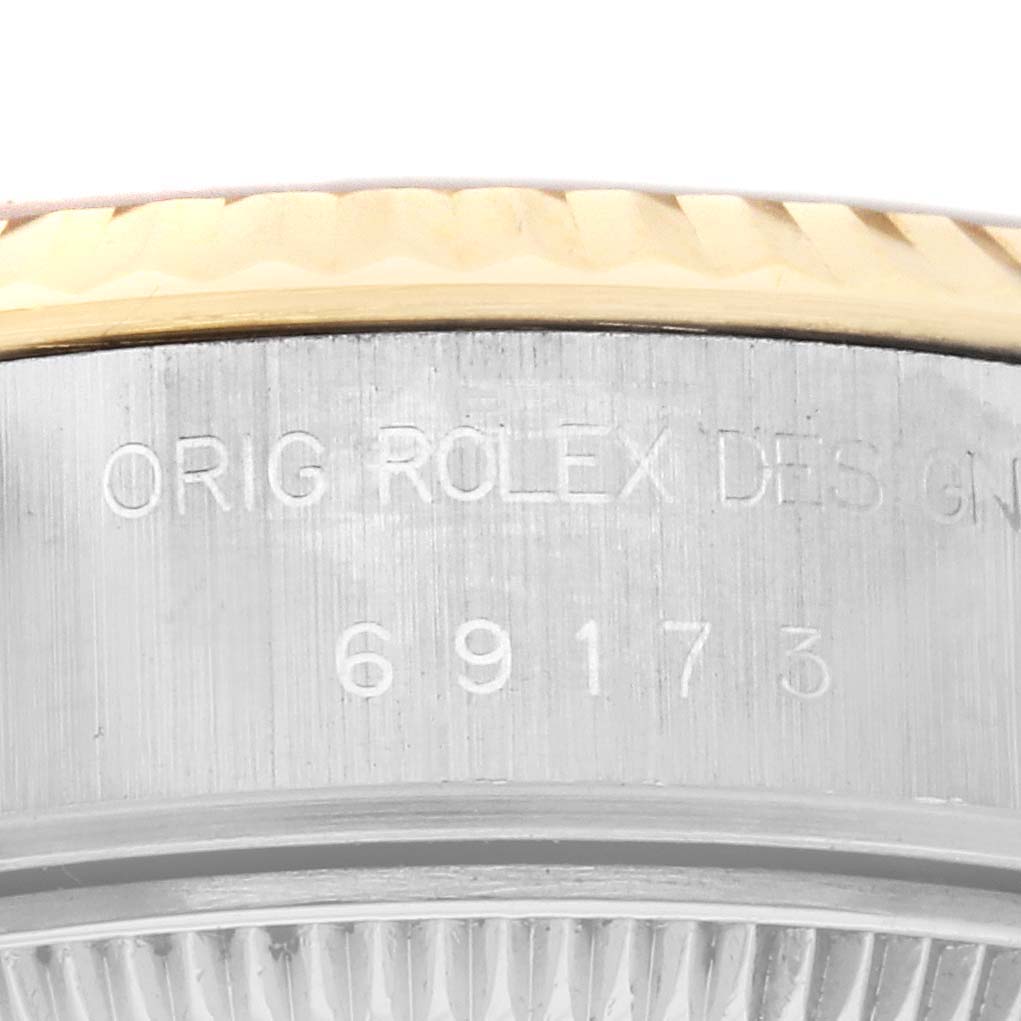 The image shows a close-up of the Rolex Datejust 69173 Women
s Steel and Gold (two tone) Champagne Dial 69173 Women
s Steel and Gold (two tone) Champagne Dial model
s case side, showing engraved details and part of the gold bezel.