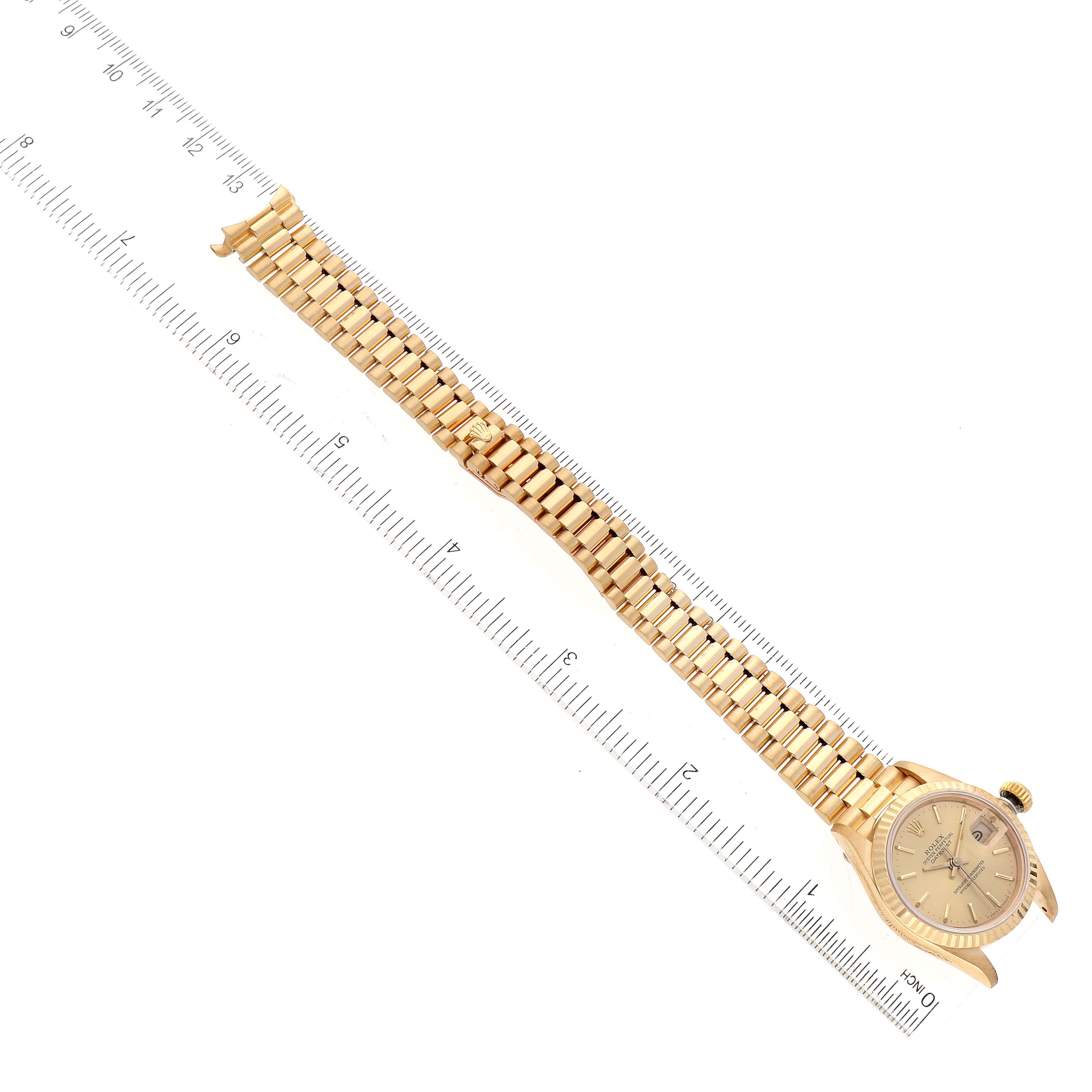 This image shows a Rolex President 69178 Women
s Yellow Gold Champagne Dial 69178 Women
s Yellow Gold Champagne Dial model watch placed diagonally along a ruler, displaying its face and bracelet.