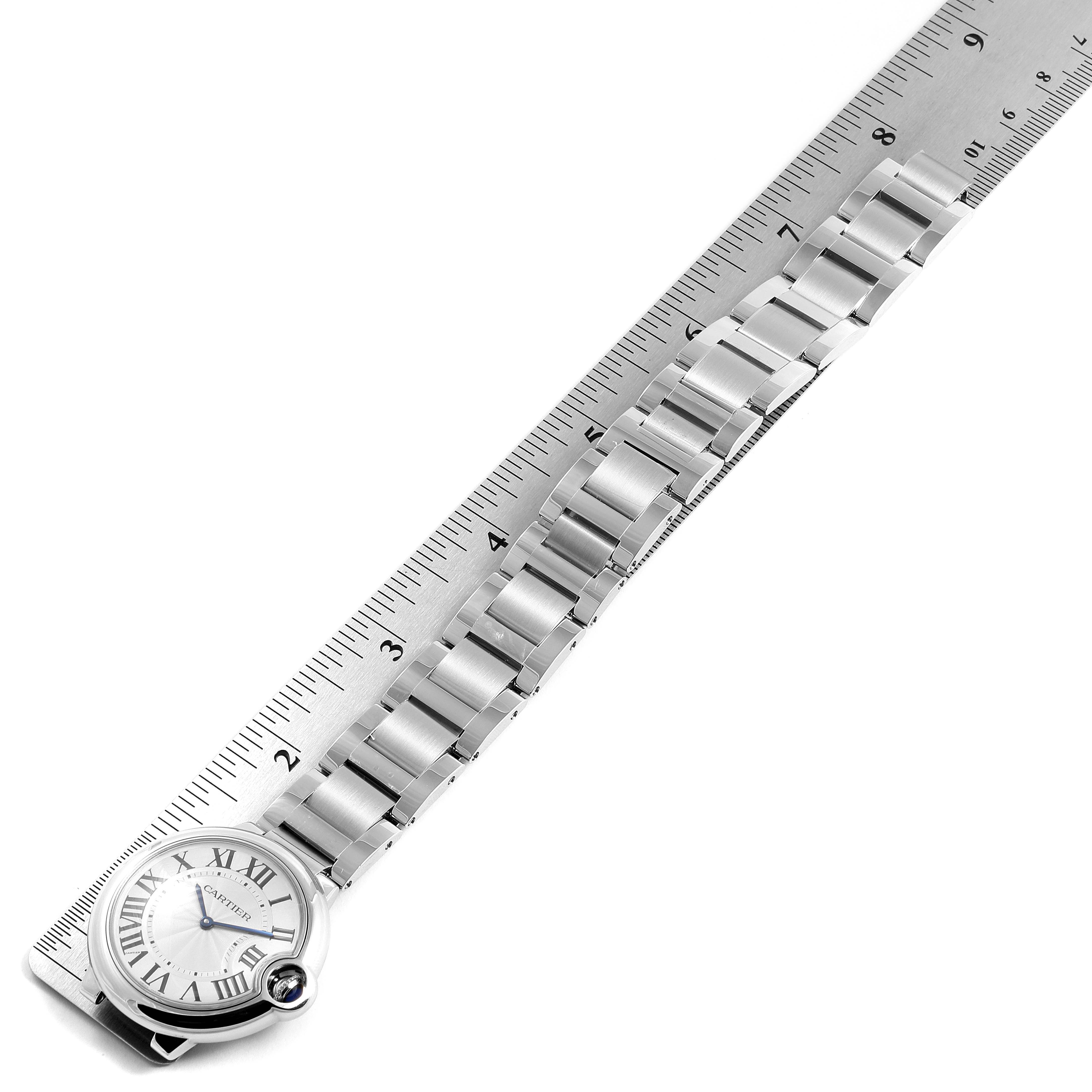 The image shows a Ballon Bleu de Cartier watch, including its face and bracelet, aligned with a metal ruler.