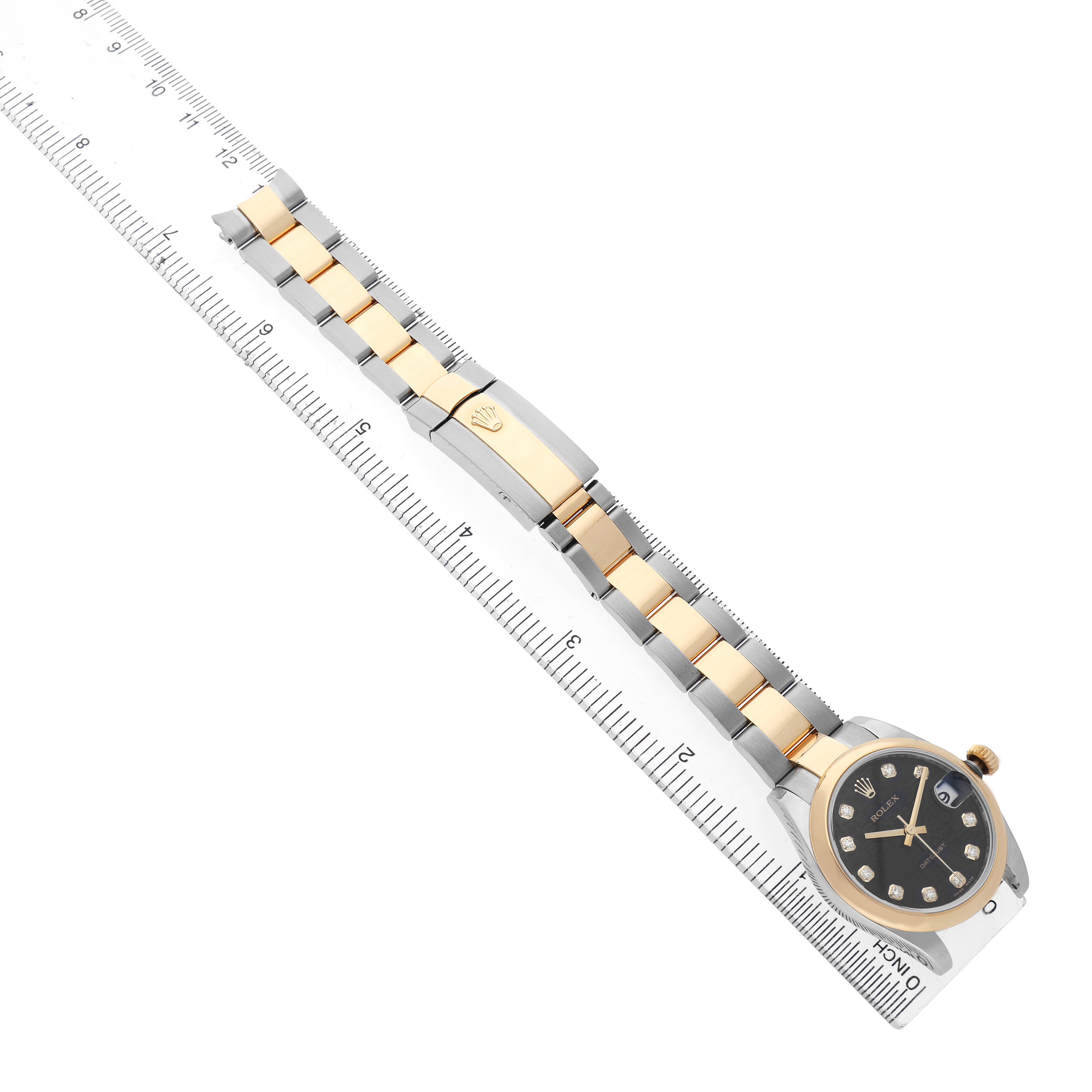 The Rolex Mid-Size 178243 Women's Steel and Gold (two tone) Black Dial watch is shown from a top view, highlighting the dial, band, and clasp alongside a ruler for scale.