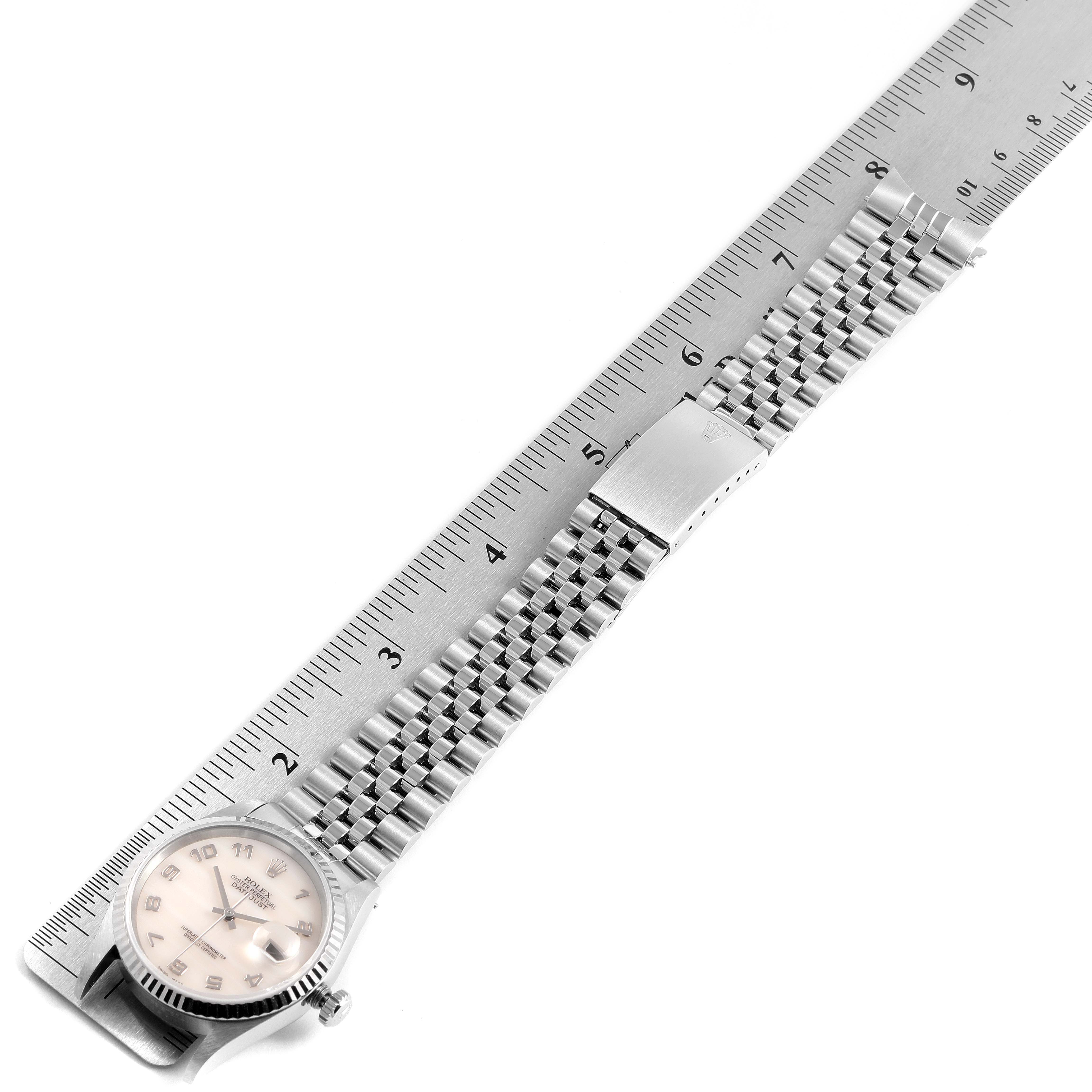 The Rolex Datejust 16234 Men's Stainless Steel Mother of Pearl Dial 16234 Men's Stainless Steel Mother of Pearl Dial watch is shown laid flat next to a ruler, featuring its face and metal bracelet.