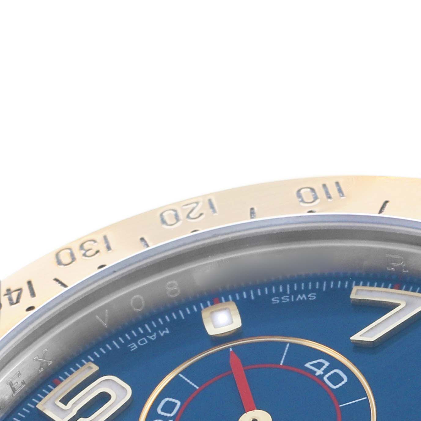 The image shows a close-up angle of the Rolex Daytona 116523 Men's Steel and Gold (two tone) Blue Dial's bezel and part of the dial with Arabic numerals.