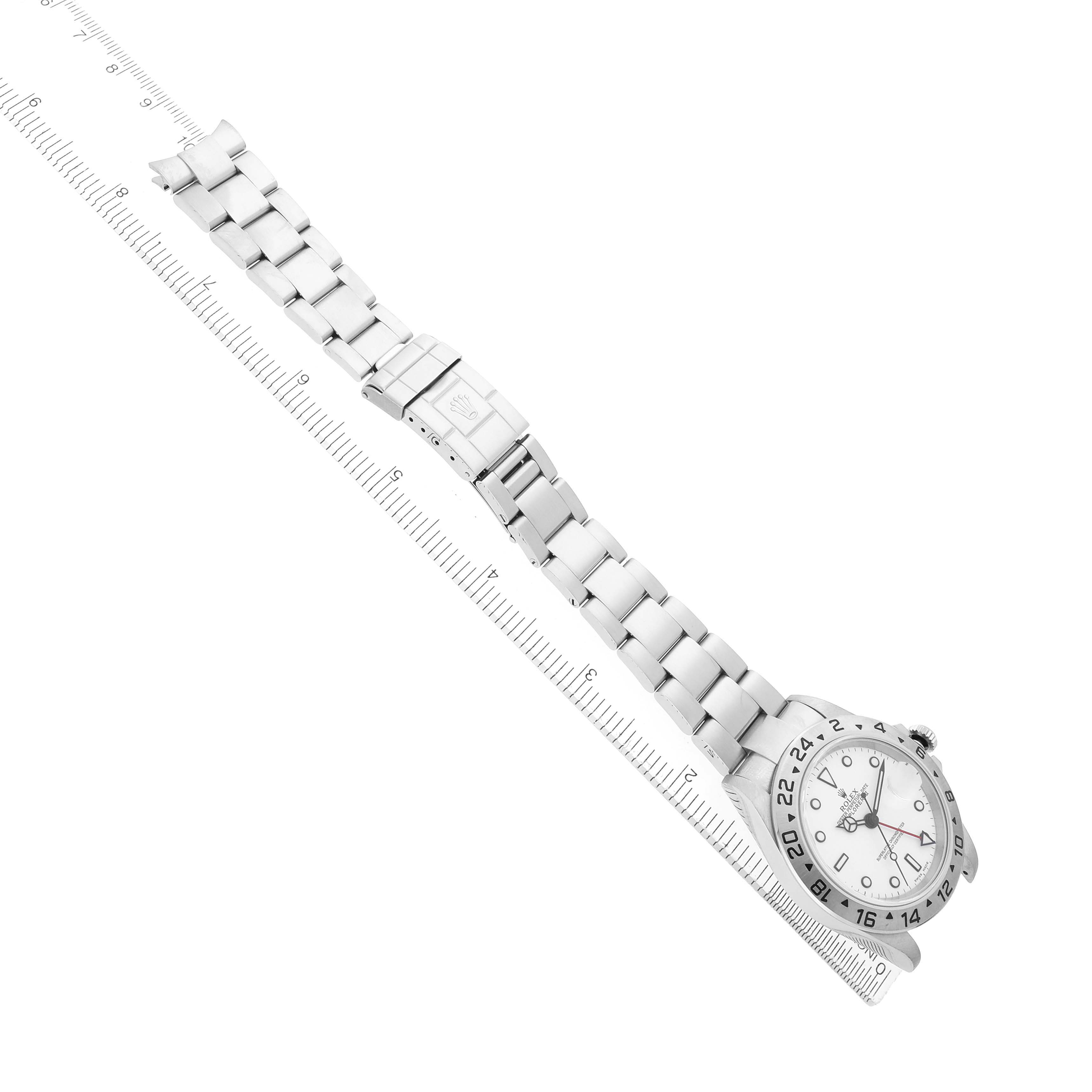 The Rolex Explorer 16570 Men's Stainless Steel White Dial watch is shown from an overhead view, displaying the face, bracelet, and clasp next to a ruler for scale.