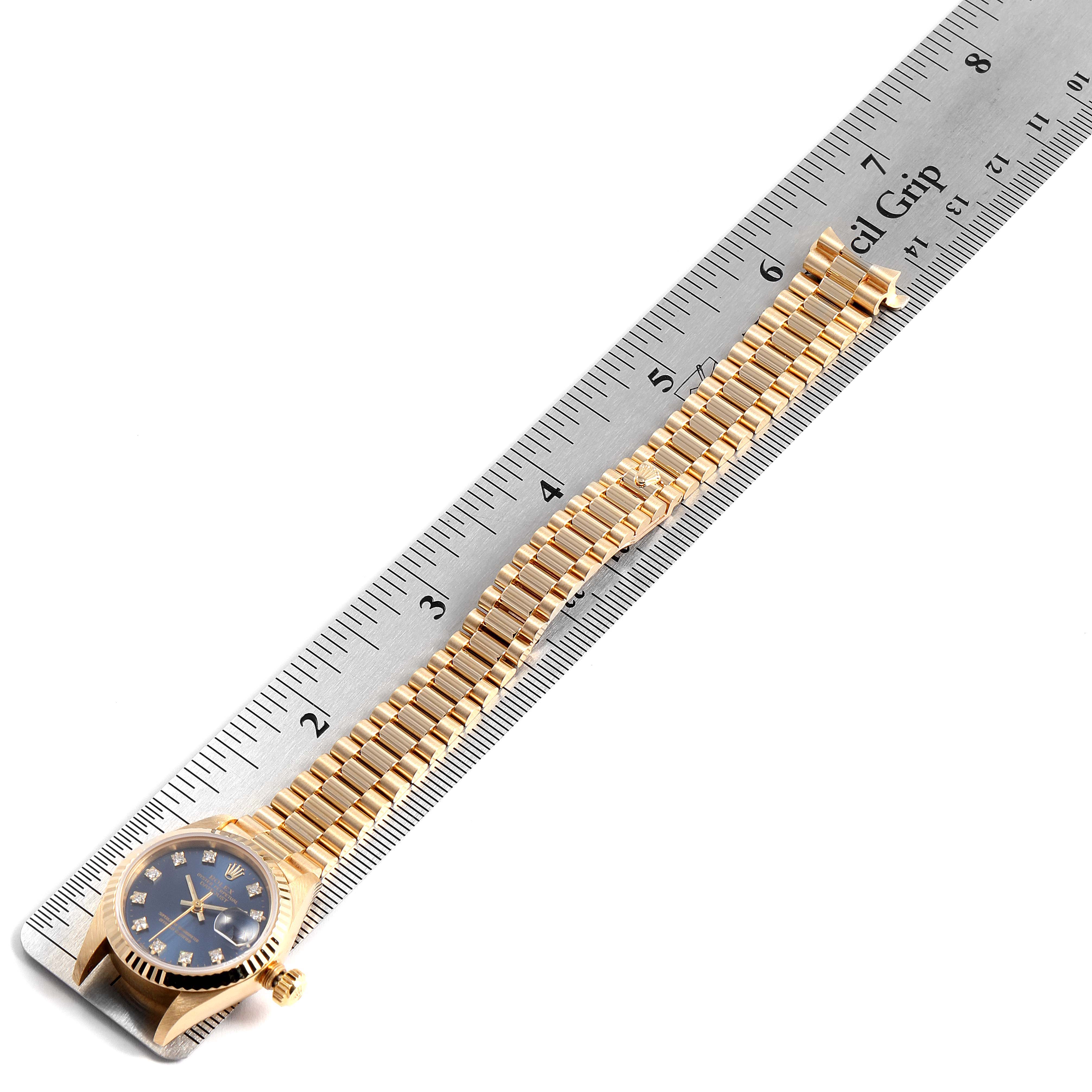 The Rolex President 69178 Women
s Yellow Gold Blue Dial 69178 Women
s Yellow Gold Blue Dial model watch is shown from a top-down angle alongside a ruler, highlighting its face and bracelet.