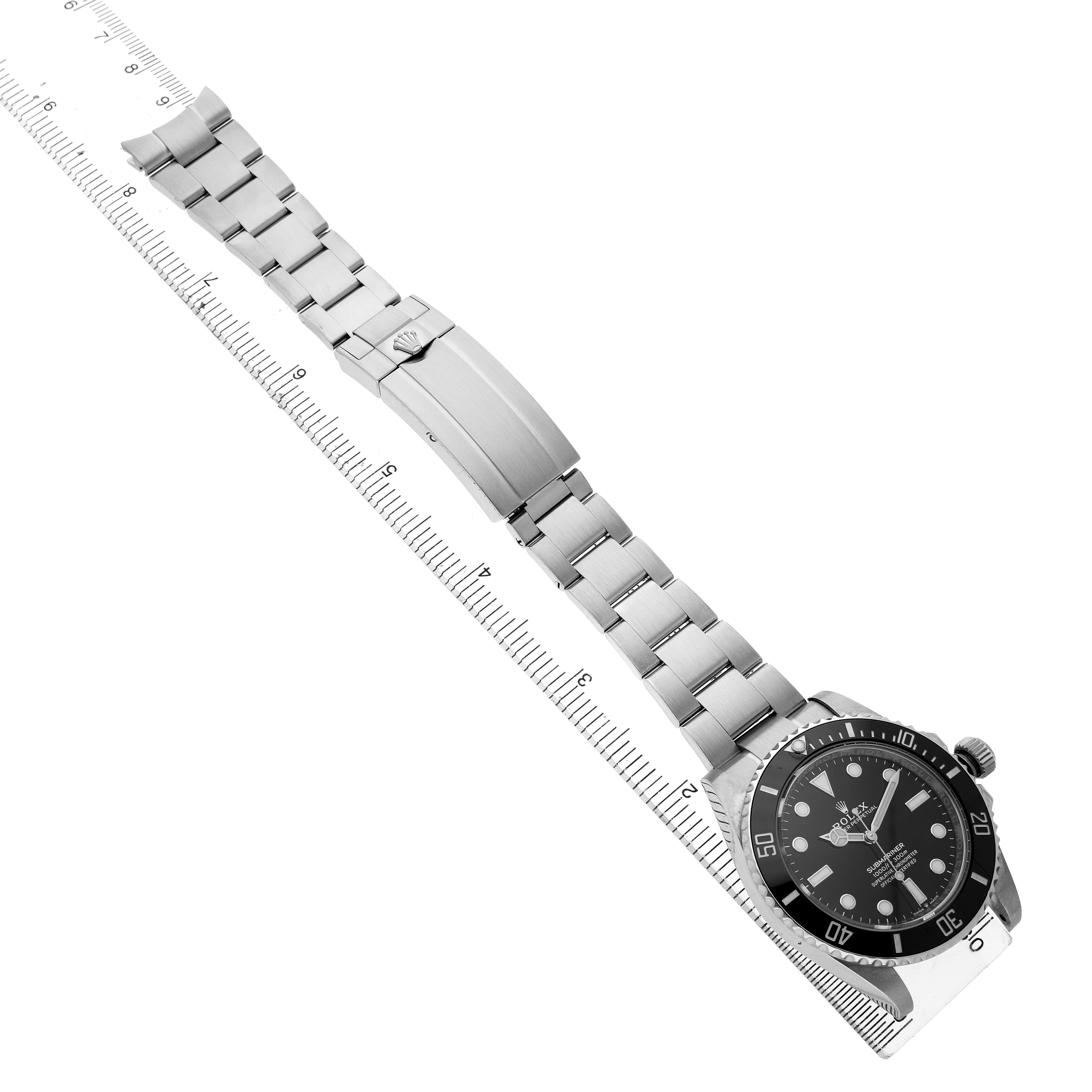 The image shows a Rolex Submariner 124060 Men's Stainless Steel Black Dial watch at a top-down angle, highlighting the bracelet, clasp, and dial alongside a ruler.