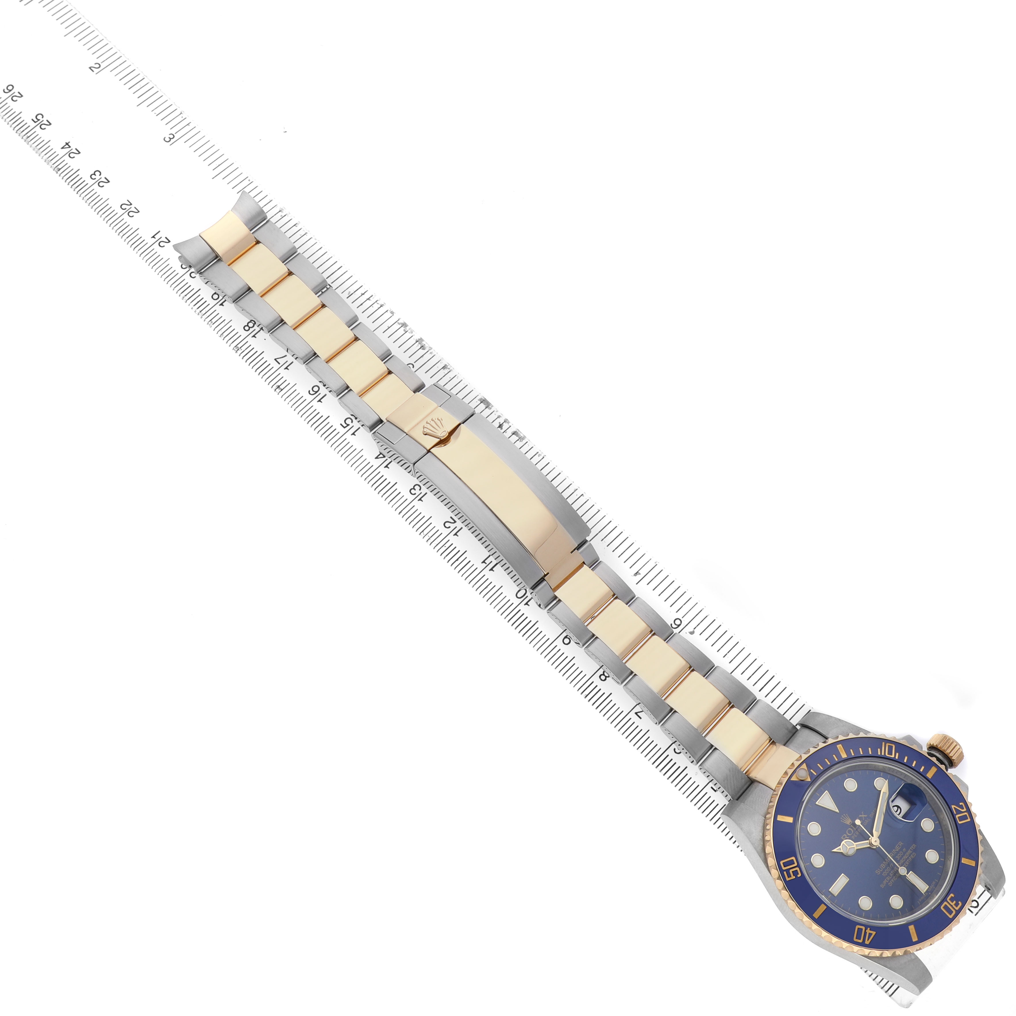 The Rolex Submariner 116613 Men's Steel and Gold (two tone) Blue Dial watch is shown from an overhead angle, displaying the bracelet, clasp, and face alongside a measuring ruler.