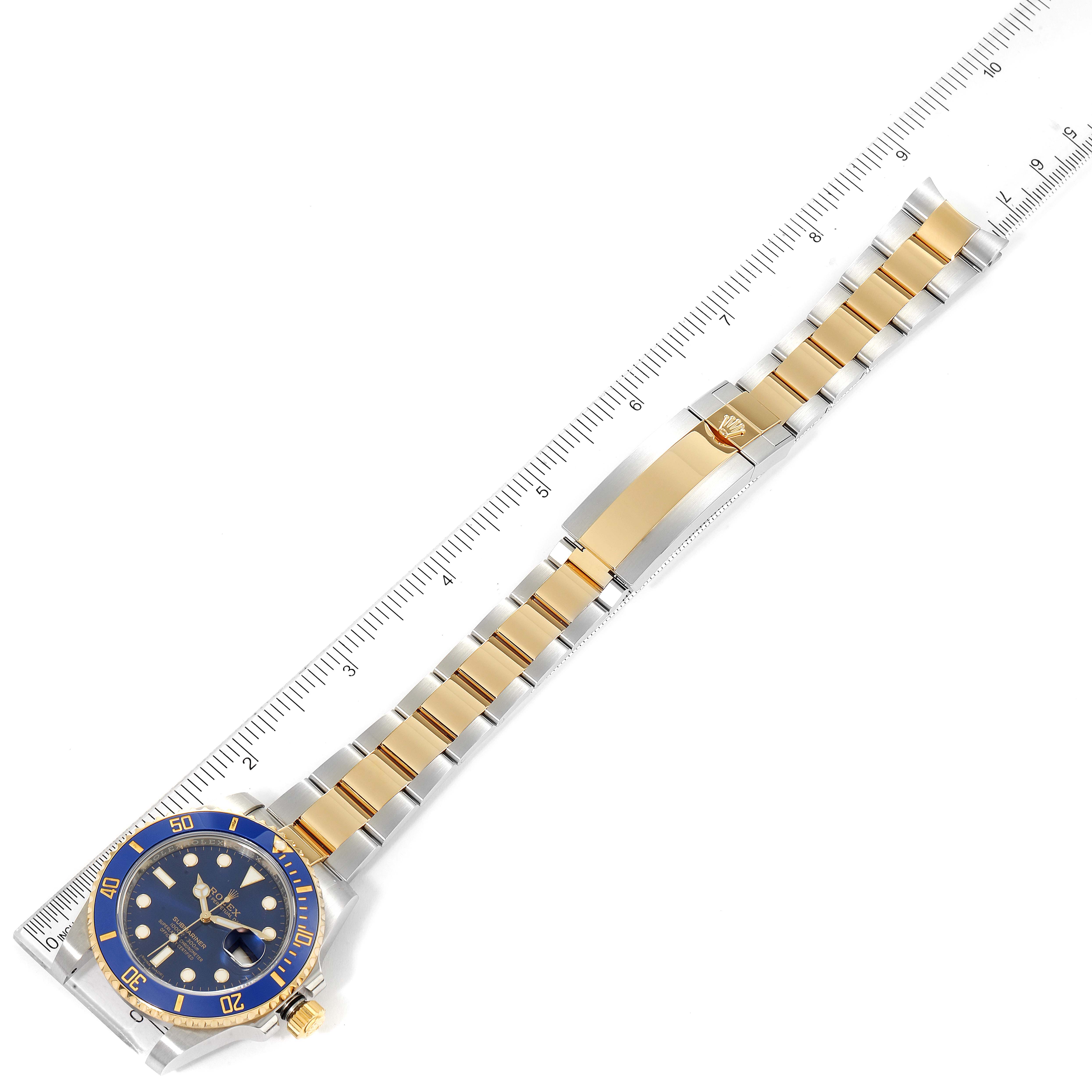 This image shows a Rolex Submariner 116613 Men's Steel and Gold (two tone) Blue Dial 116613 Men's Steel and Gold (two tone) Blue Dial watch laid flat alongside a ruler, displaying its face, bezel, bracelet, and clasp.