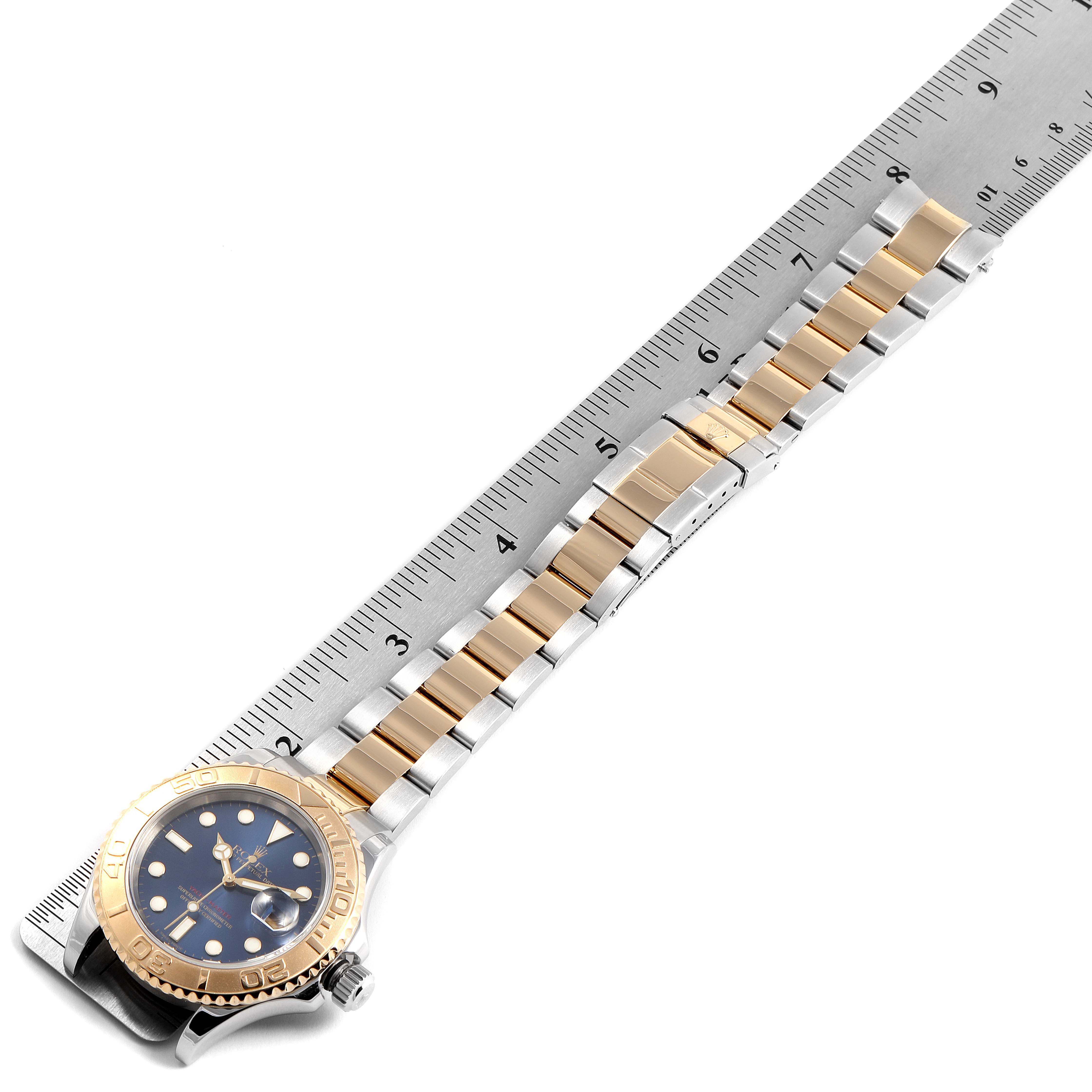 The image shows a Rolex Yacht-Master 16623 Men
s Steel and Gold (two tone) Blue Dial 16623 Men
s Steel and Gold (two tone) Blue Dial watch from a top-down angle, displaying its face, bezel, and bracelet alongside a ruler.