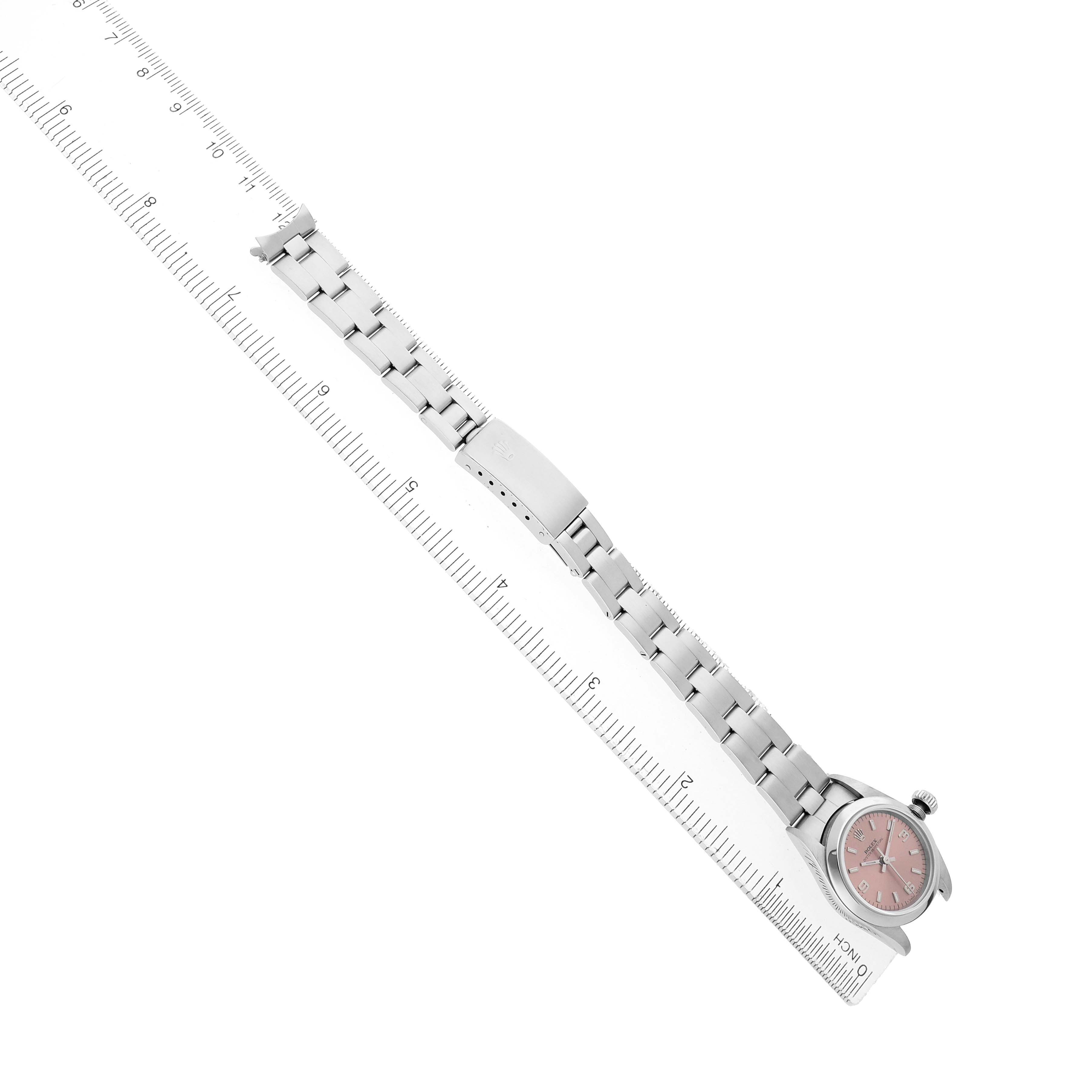 The Rolex Oyster Perpetual 67180 Women's Stainless Steel Pink Dial watch is shown from a top-down angle, displaying the band and pink dial alongside a measuring ruler.