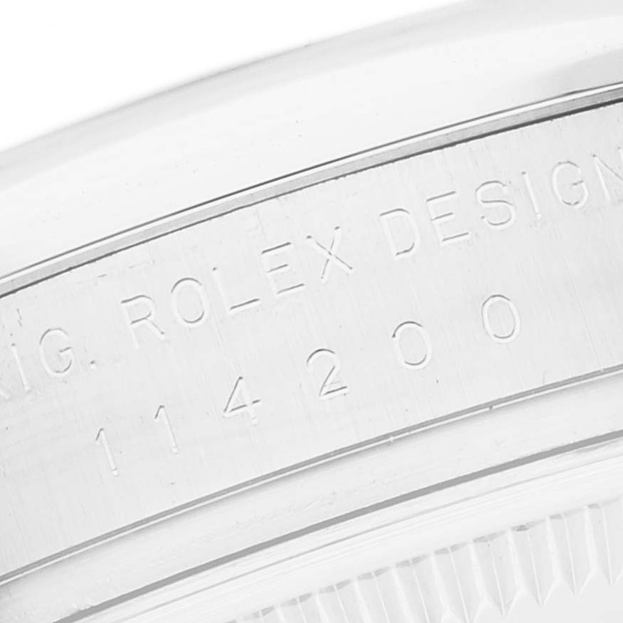 The image shows a close-up of the engraved case back of a Rolex Oyster Perpetual 114200 Men's Stainless Steel White Dial 114200 Men's Stainless Steel White Dial model, focusing on the serial number.