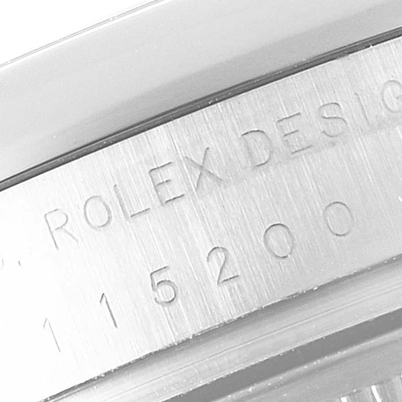 The image shows a close-up, angled view of the engraved serial number and the "Rolex Design" inscription on a Rolex Date 115200 Men's Stainless Steel Black Dial 115200 Men's Stainless Steel Black Dial model watch.