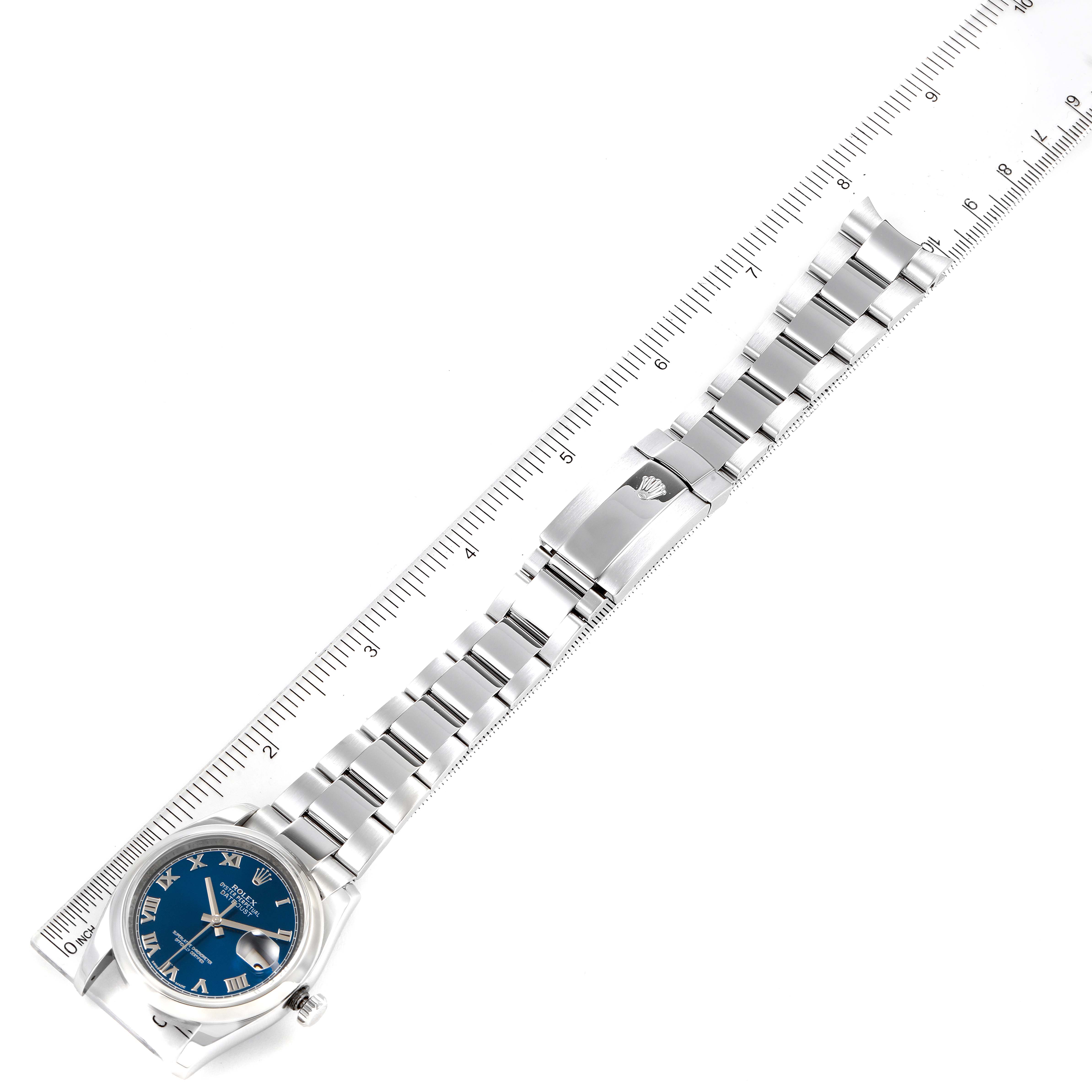 The image shows a Rolex Datejust 116200 Men's Stainless Steel Blue Dial 116200 Men's Stainless Steel Blue Dial watch from a top-down angle, highlighting its blue dial, metal bracelet, and clasp next to a ruler.