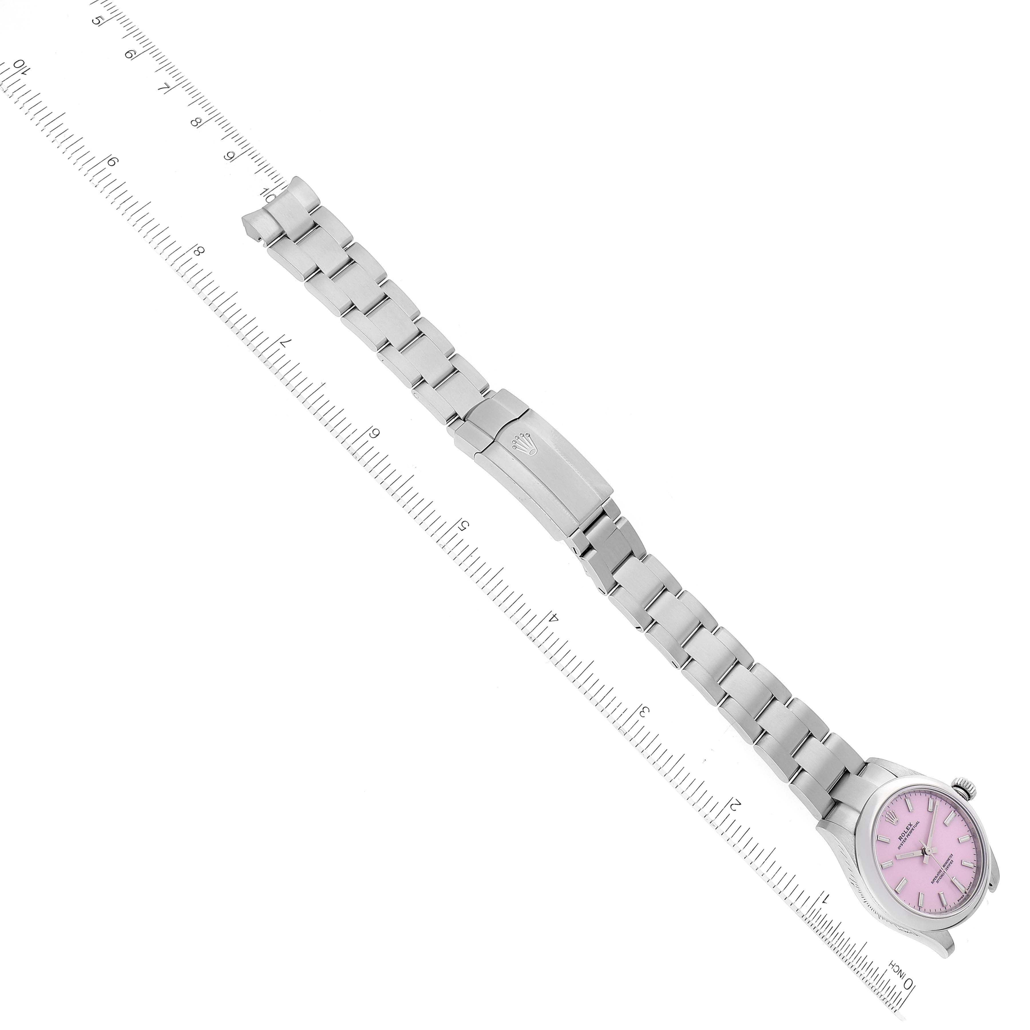 The image shows a Rolex Mid-Size 277200 Women's Stainless Steel Pink Dial 277200 Women's Stainless Steel Pink Dial watch with a pink dial and a metal bracelet, positioned diagonally with a ruler for scale.