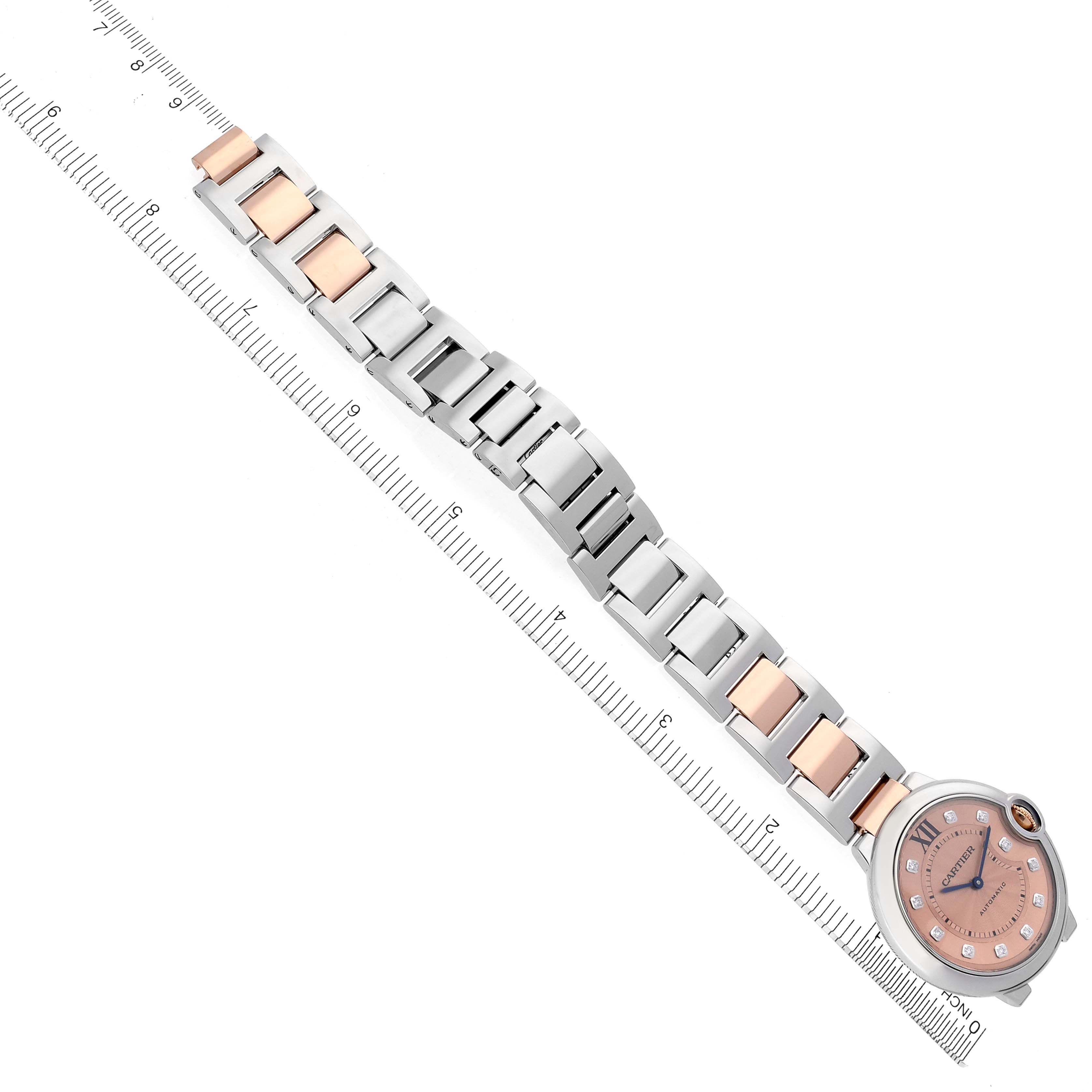 The Cartier Ballon Bleu WE902054 Women's Steel and Gold (two tone) Pink Dial WE902054 Women's Steel and Gold (two tone) Pink Dial watch is shown from above, highlighting its band and round face beside a ruler for size reference.