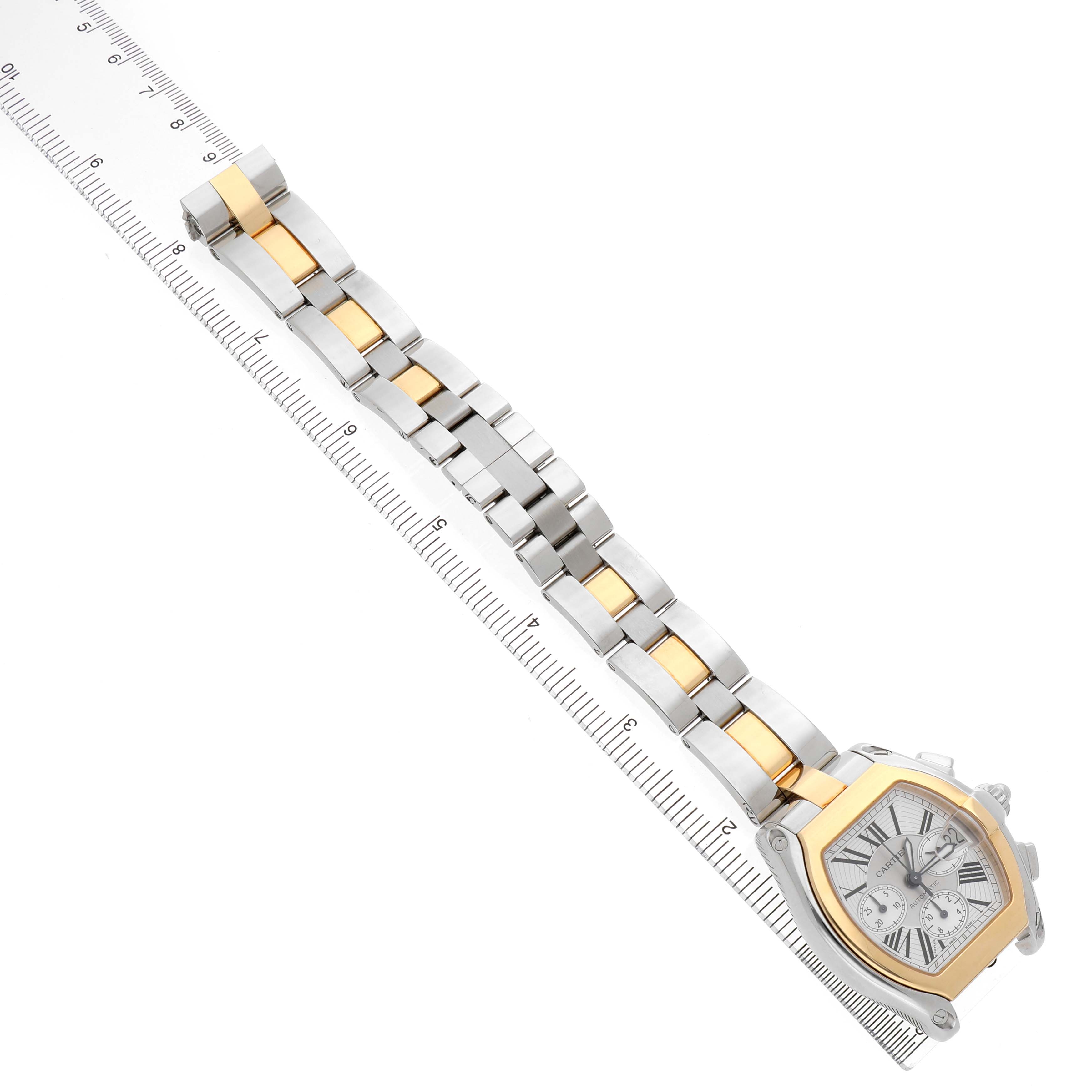 The Cartier Roadster W62027Z1 Men's Steel and Gold (two tone) Silver Dial watch is shown diagonally, highlighting its face and two-tone bracelet alongside a ruler for scale.