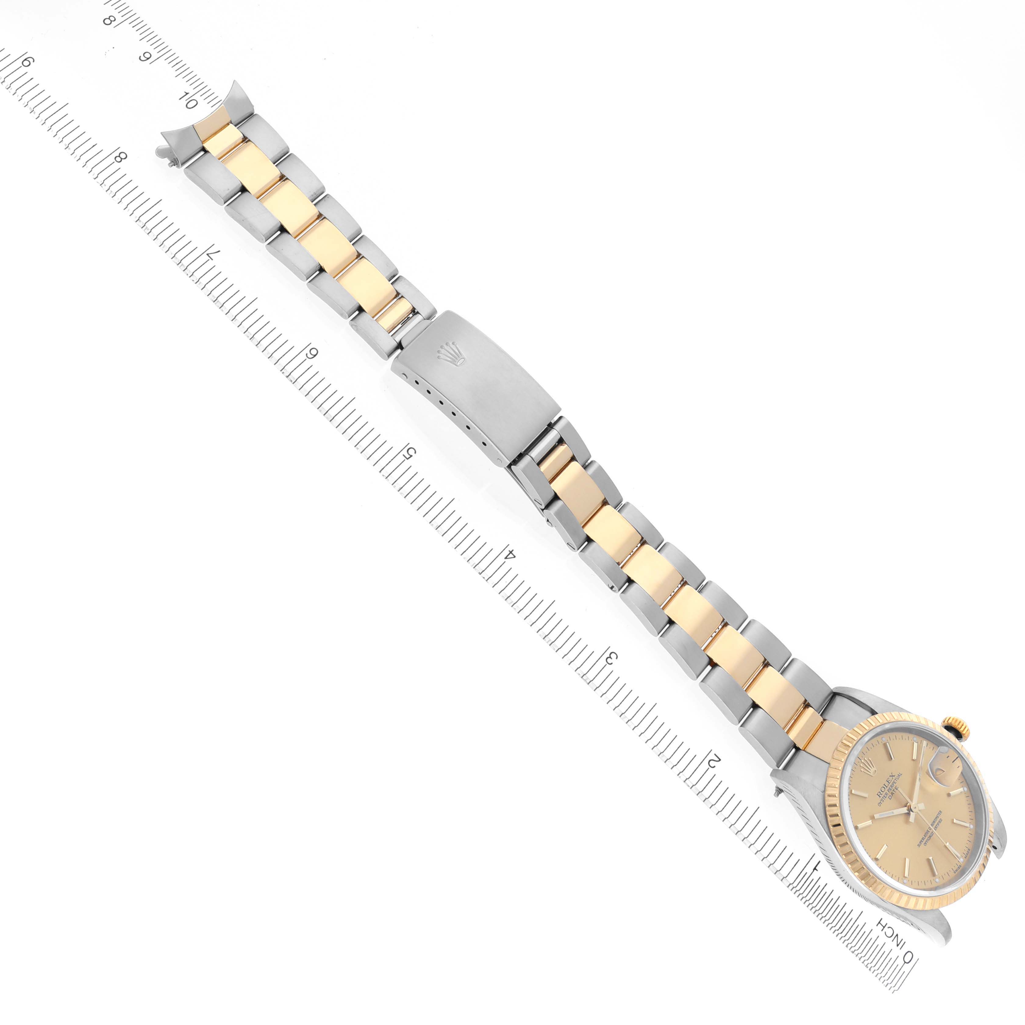 The image shows a Rolex Date 15223 Men's Steel and Gold (two tone) Champagne Dial 15223 Men's Steel and Gold (two tone) Champagne Dial model watch from an overhead angle, displaying the face, bracelet, and clasp on a ruler.