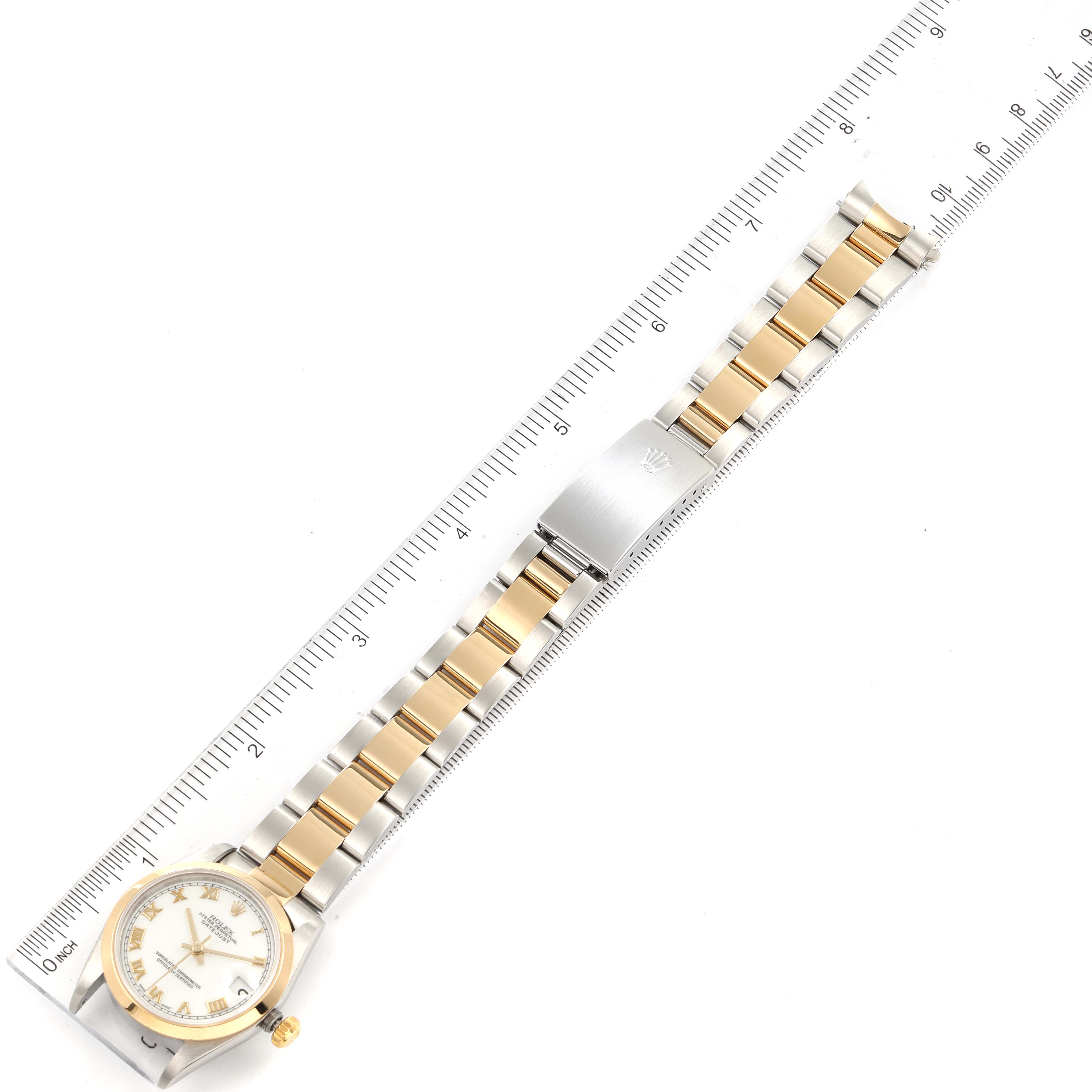 The image shows a top-down view of the entire Rolex Mid-Size 78243 Women
s Steel and Gold (two tone) White Dial 78243 Women
s Steel and Gold (two tone) White Dial watch, including the band, dial, and clasp, against a ruler.