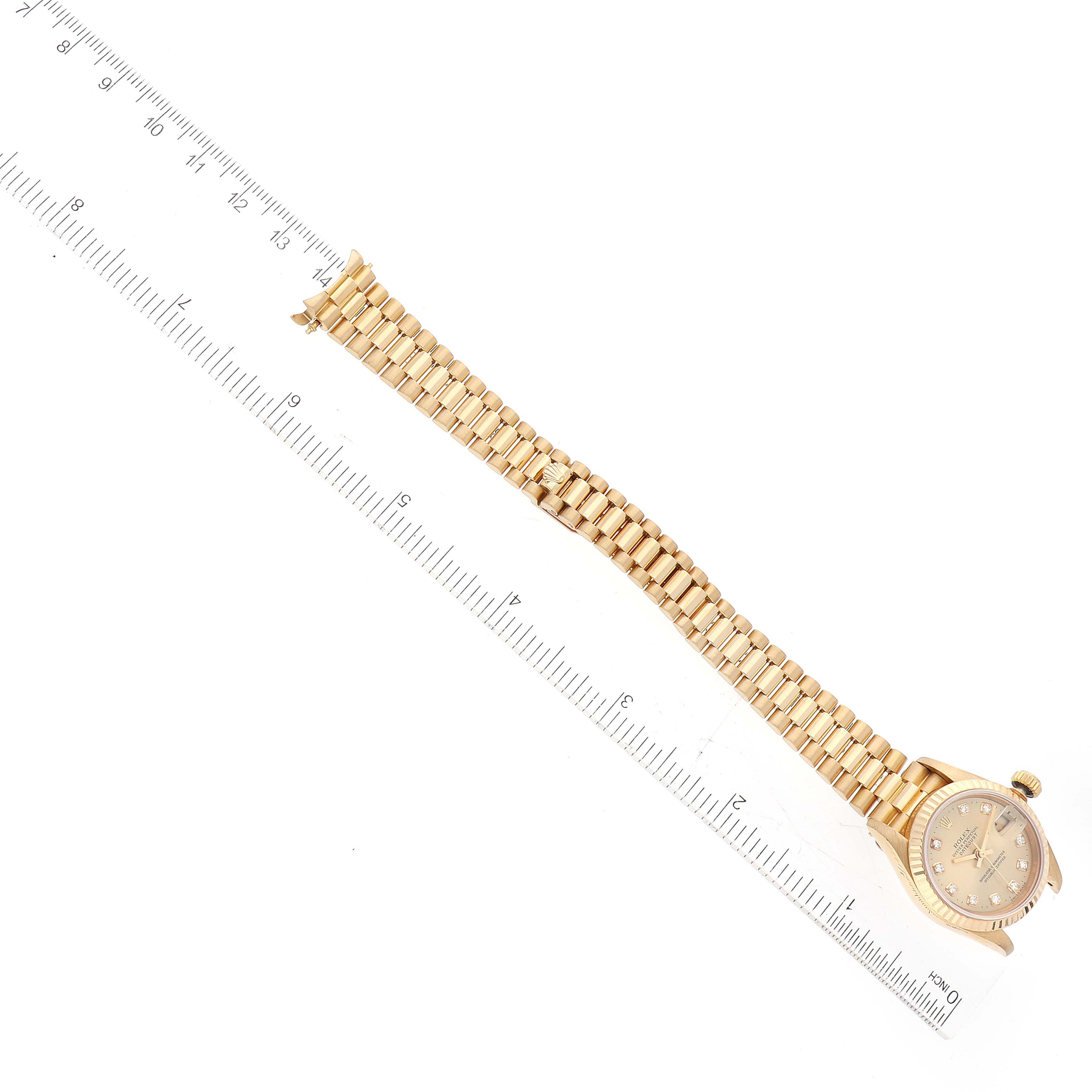 This image shows a top view of a Rolex President 69178 Women's Yellow Gold Champagne Dial 69178 Women's Yellow Gold Champagne Dial model watch with a gold case and band next to a ruler.