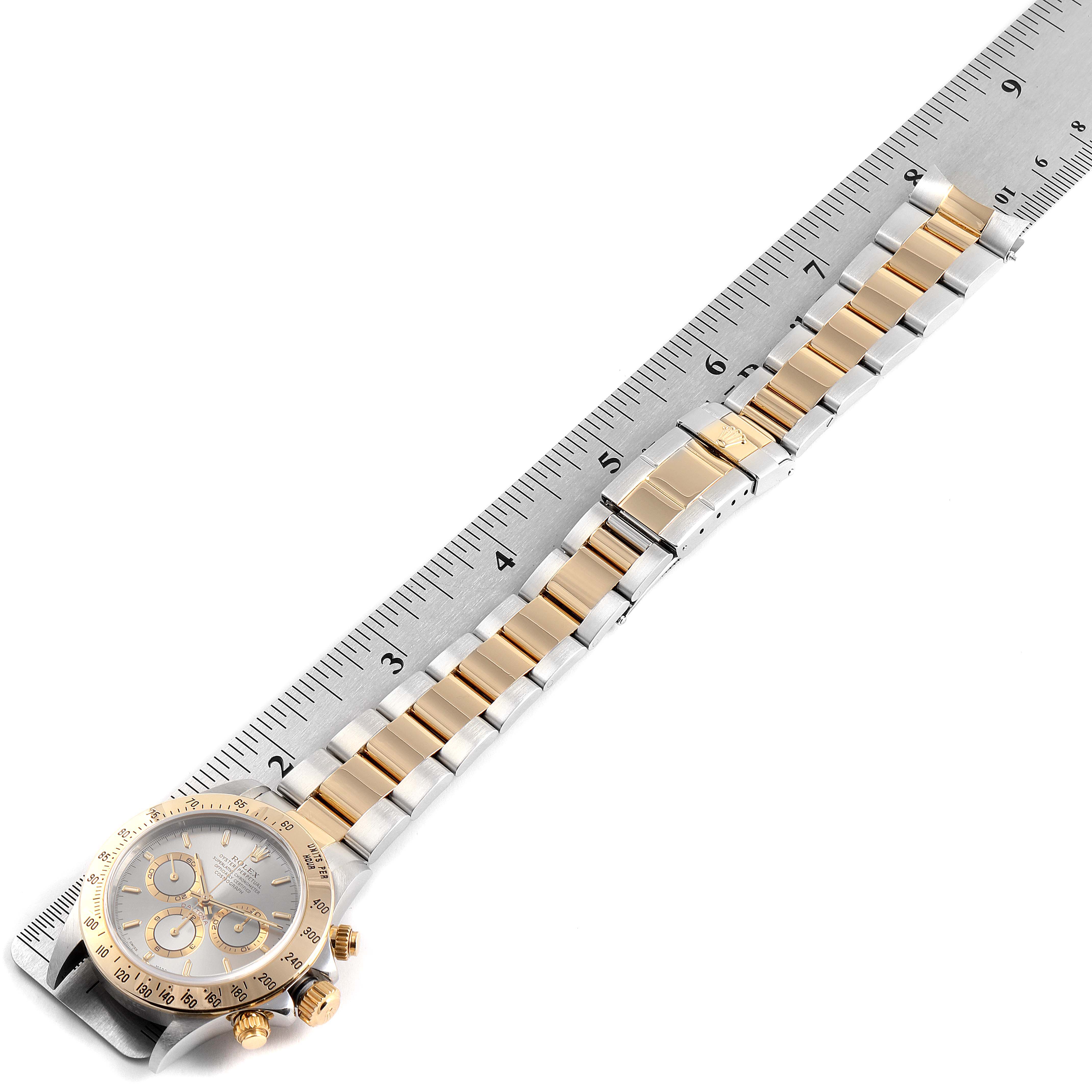 The image shows a Rolex Daytona 16523 Men's Steel and Gold (two tone) Grey Dial 16523 Men's Steel and Gold (two tone) Grey Dial watch laid horizontally next to a ruler, displaying the face, band, and clasp.