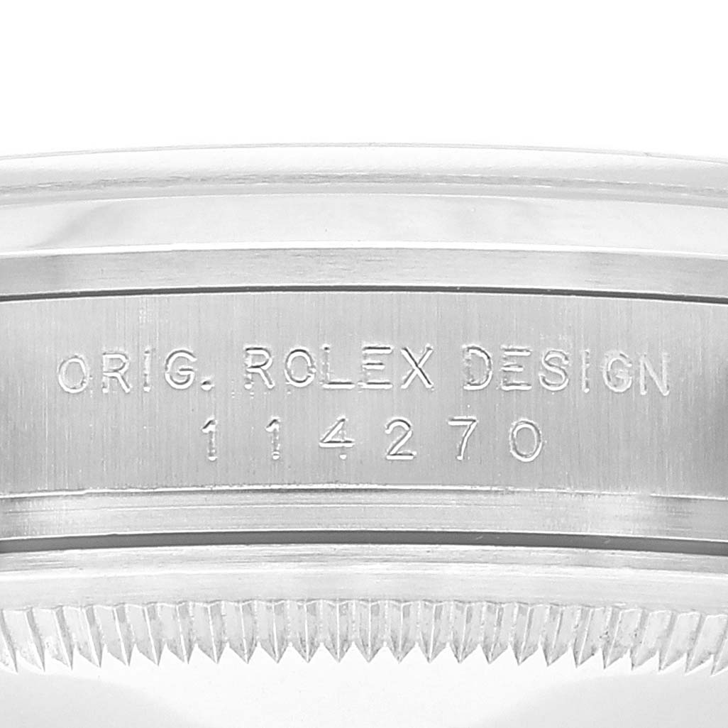 The image shows a close-up of the case side engraving of a Rolex Explorer 114270 Men
s Stainless Steel Black Dial 114270 Men
s Stainless Steel Black Dial model, indicating "ORIG. ROLEX DESIGN" and the reference number "114270".