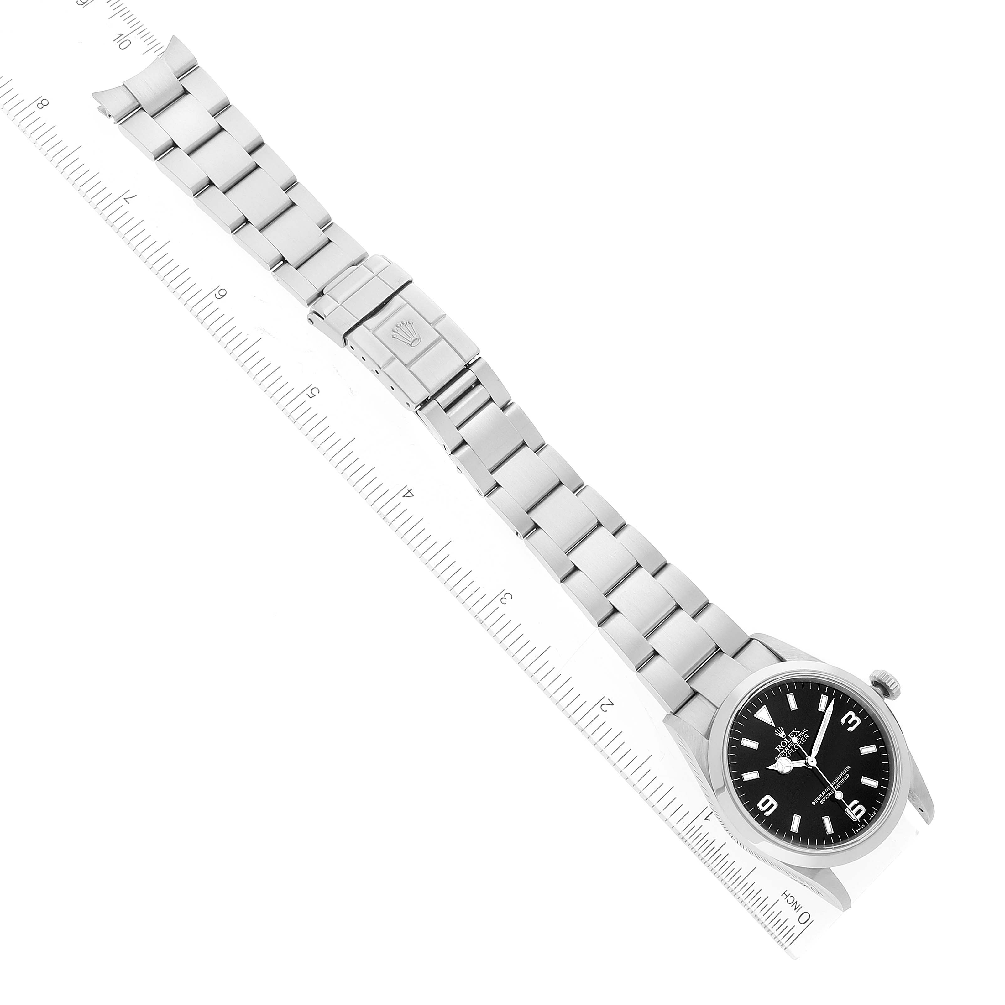 The image shows a top-down view of a Rolex Explorer 114270 Men
s Stainless Steel Black Dial 114270 Men
s Stainless Steel Black Dial watch, displaying its metal bracelet, clasp, and face along a ruler.